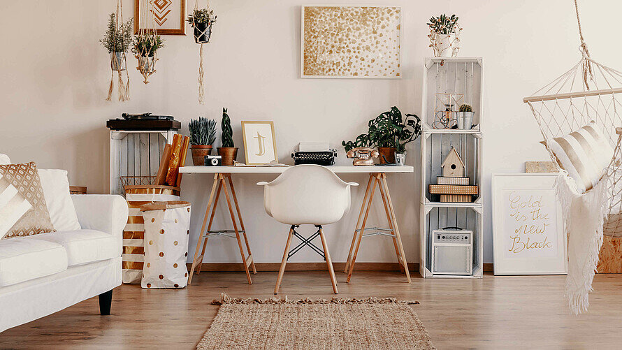 Ein Zimmer mit weißen Möbeln, Blick auf einen Schreibtisch, links ein Sofa.