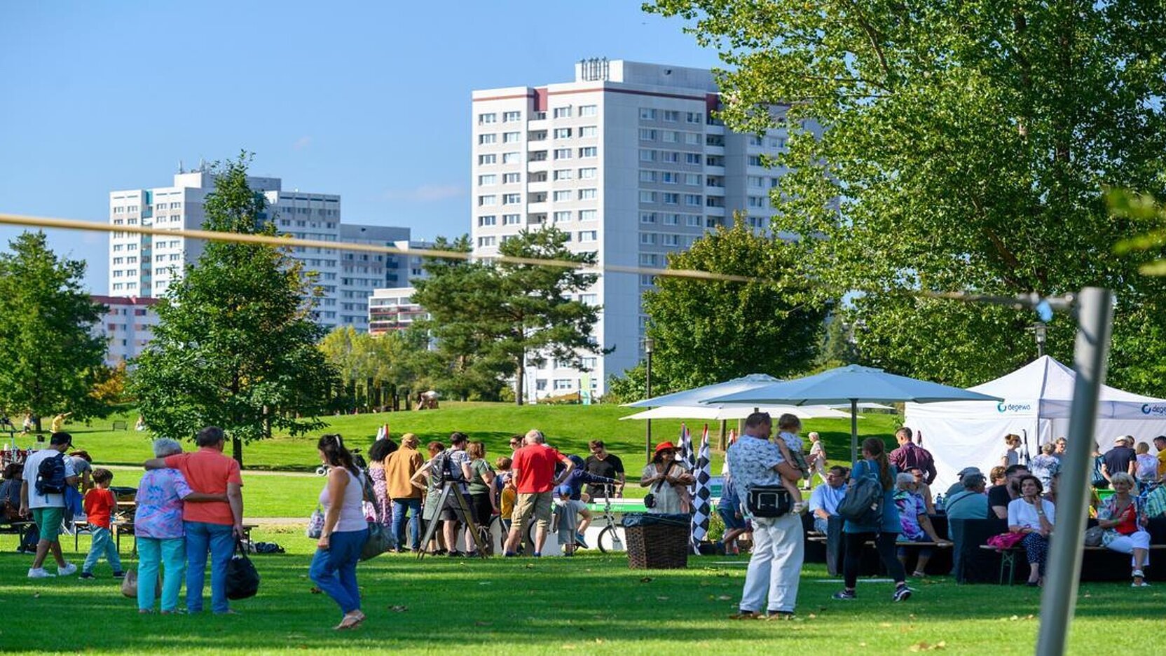 Mieter auf dem degewo-Mieterfest in den Gärten der Welt. Im Hintergrund sind Plattenbauten zu sehen. 