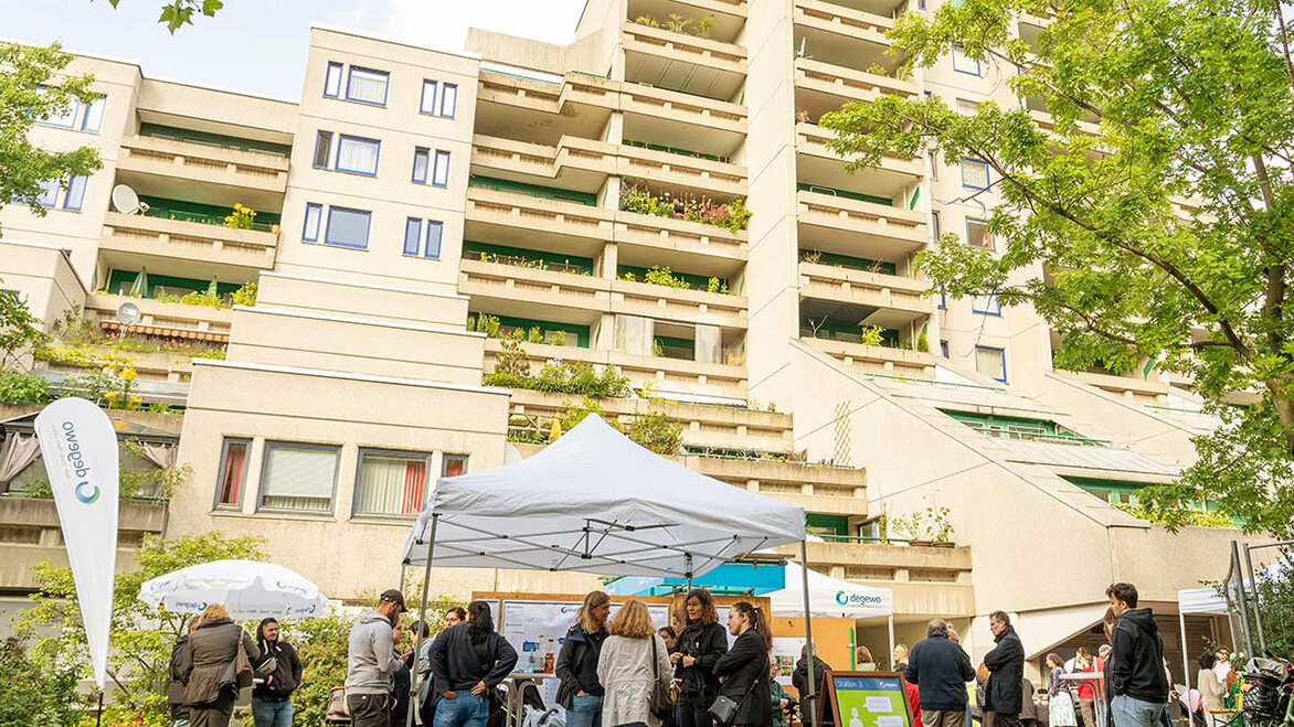 Gruppenaufnahme während der Informationsveranstaltung zur Sanierung der Schöneberger Terrassen. Mitarbeiter von degewo stehen mit Mieterinnen und Mietern vor dem Gebäude zusammen und reden.