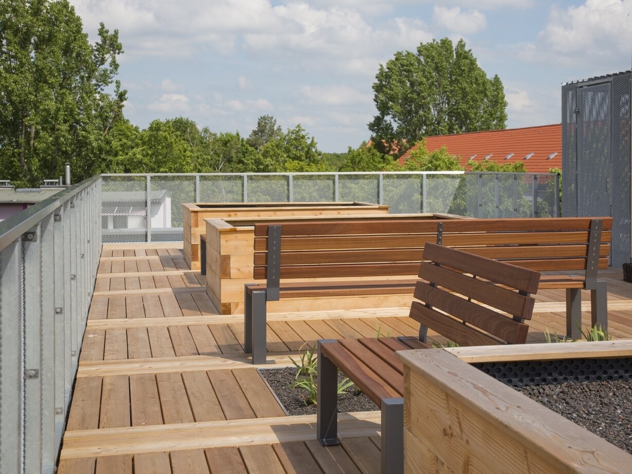 Außenansicht degewo-Neubau Karl-Pokern-Straße 30 bis 36: Terrassendach mit Sitzbänken und Hochbeeten.