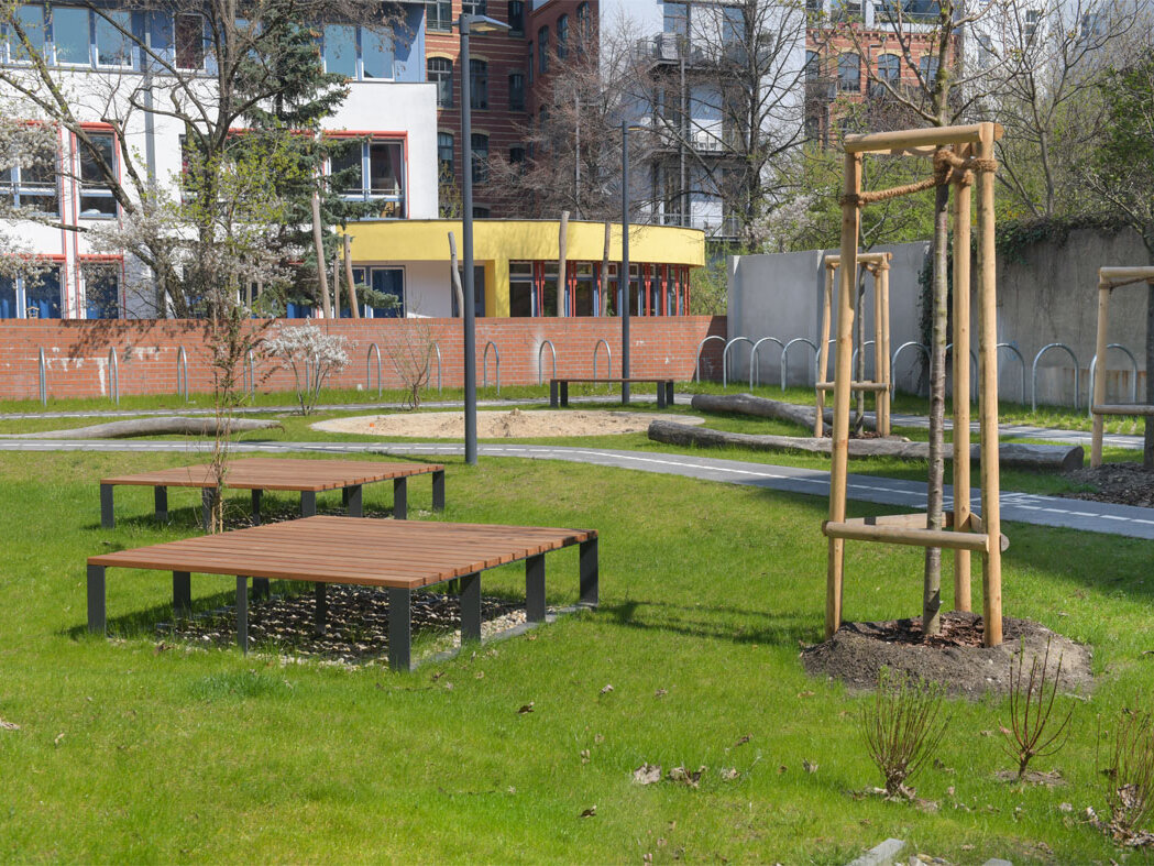 Außenansicht degewo-Neubau Lützowstraße 7: Rasenfläche mit Sitzgelegenheiten sowie neu gepflanzten Büschen und Bäumen.