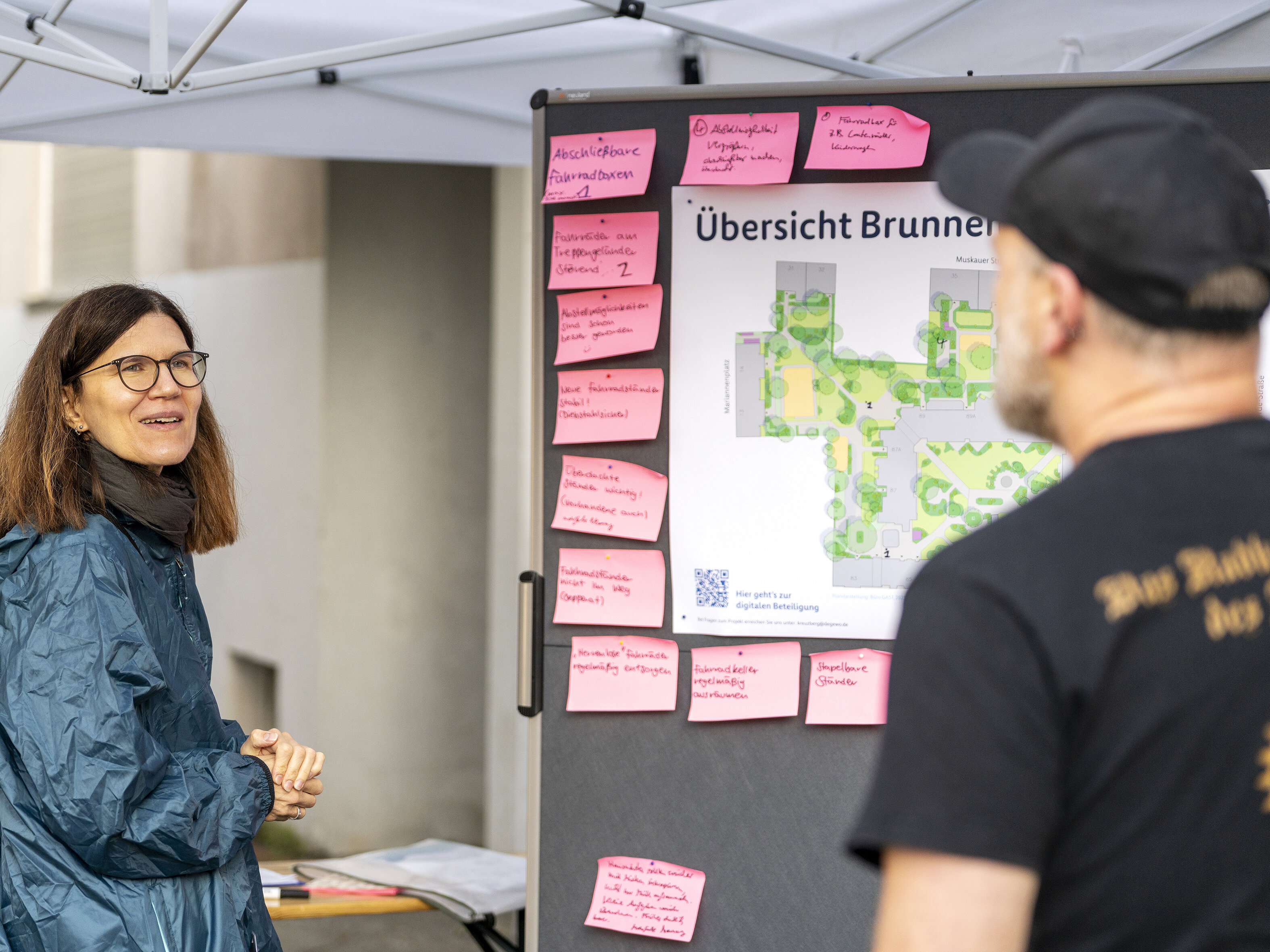 Gespräch am Beteiligungsstand: Eine Mitarbeiterin erläutert die Planungen, während pinke Notizzettel mit Anregungen an der Tafel hängen.