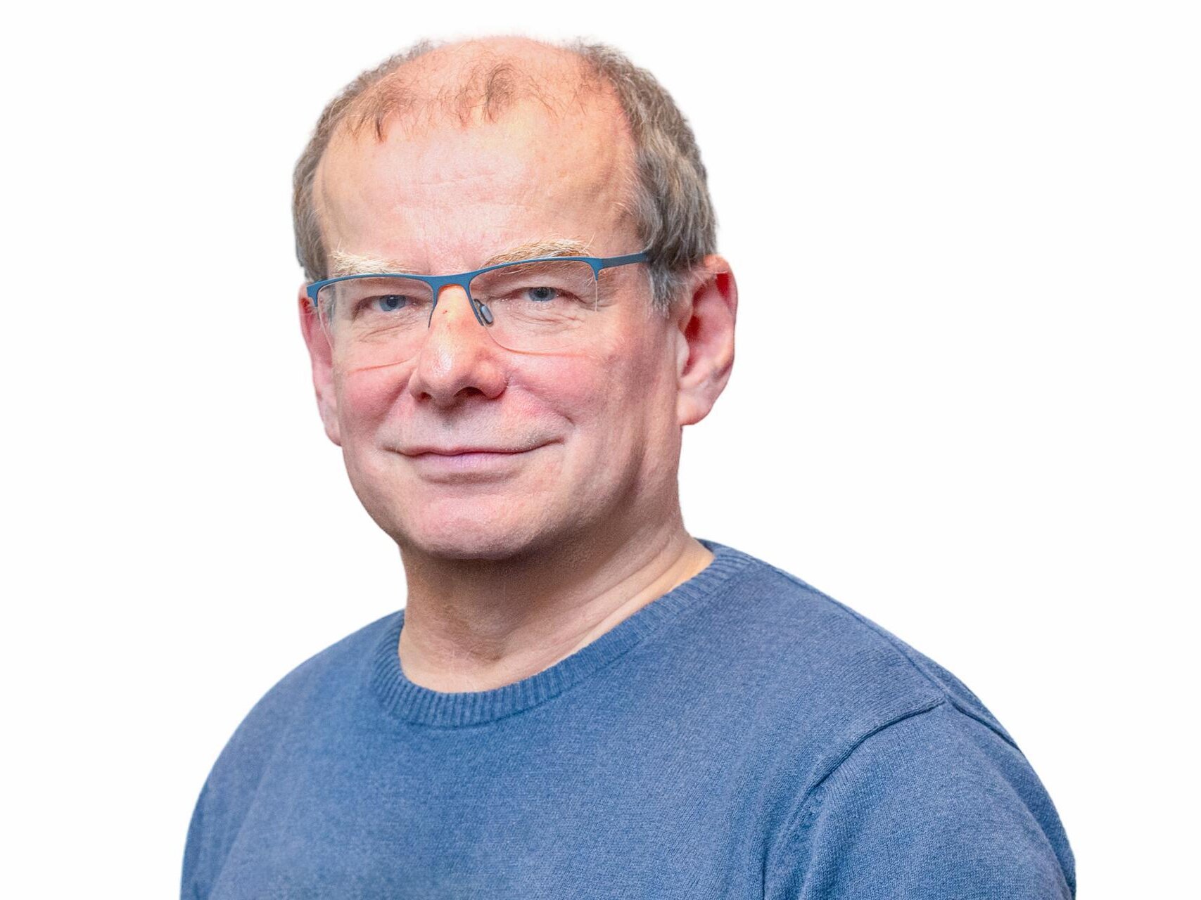 Ein älterer Herr mit dunkelblauem Pullover schaut freundlich in die Kamera.