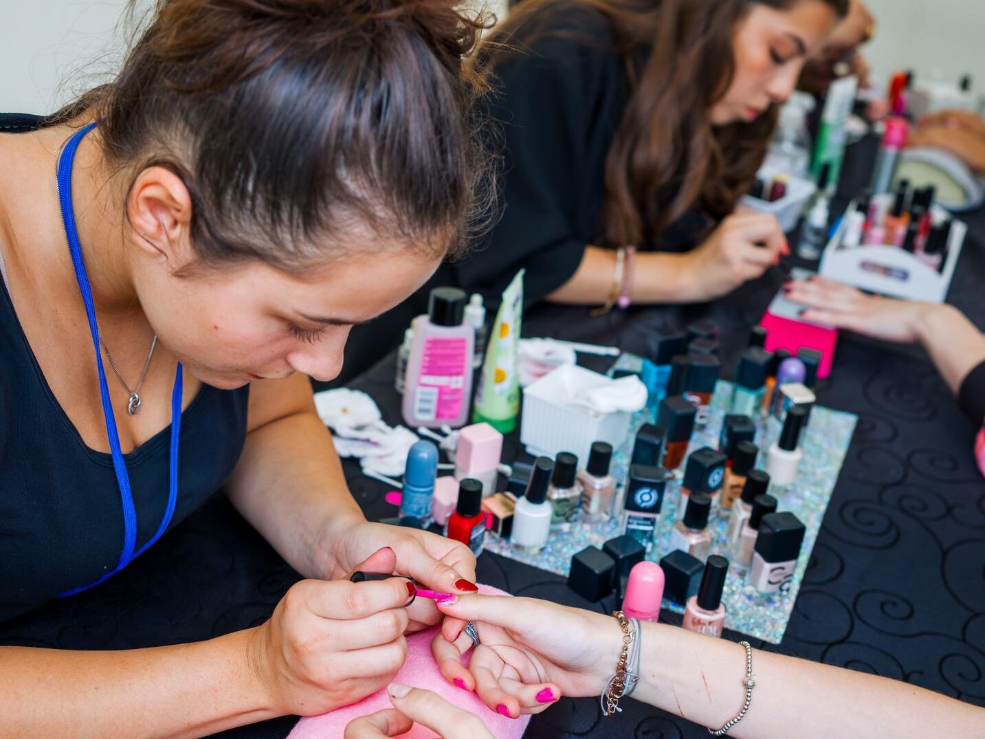 An einem Stand lackiert eine Fachkraft die Fingernägel einer Besucherin. Auf dem Tisch stehen zahlreiche Nagellacke und Pflegeprodukte; weitere Behandlungen finden im Hintergrund statt.