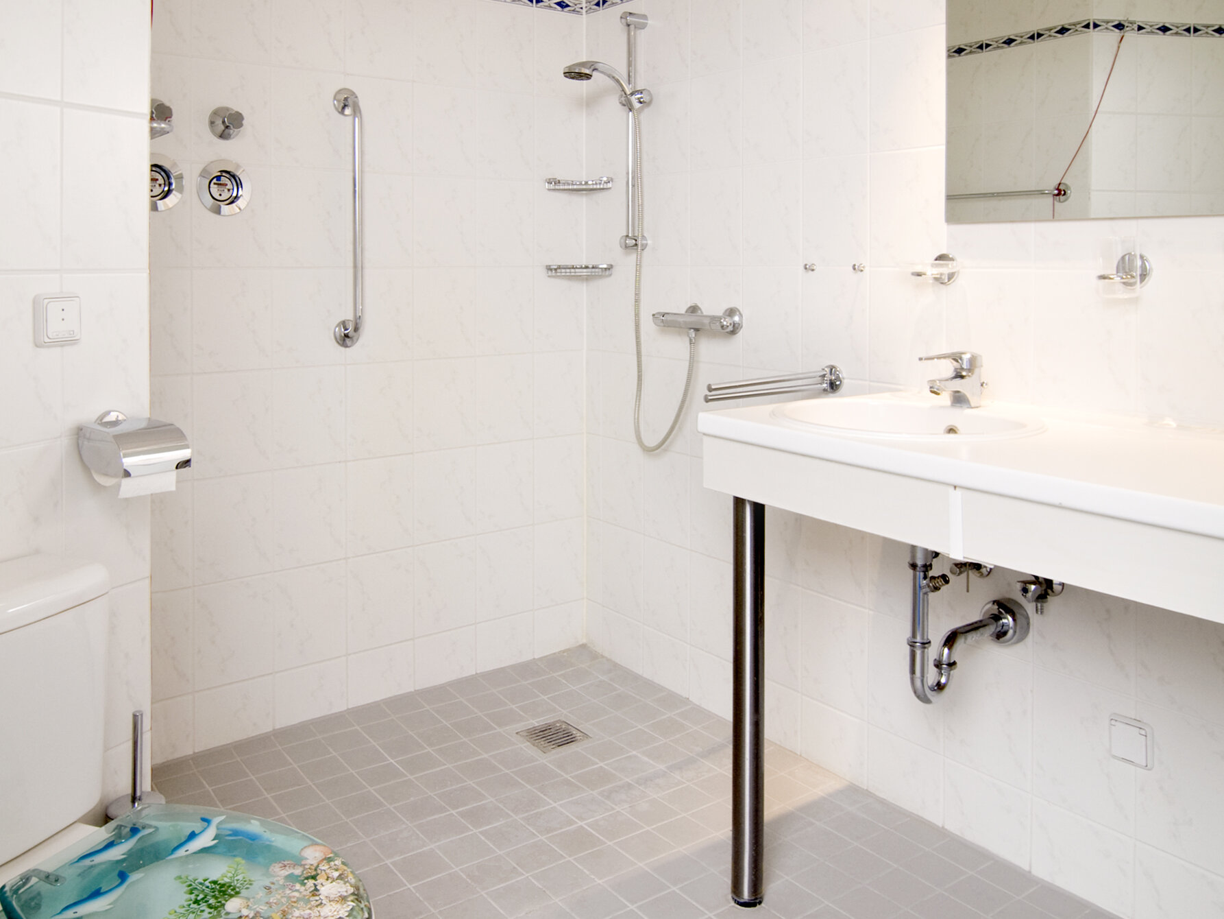 Badezimmer mit Waschbecken, Toilette und bodengleicher Dusche.