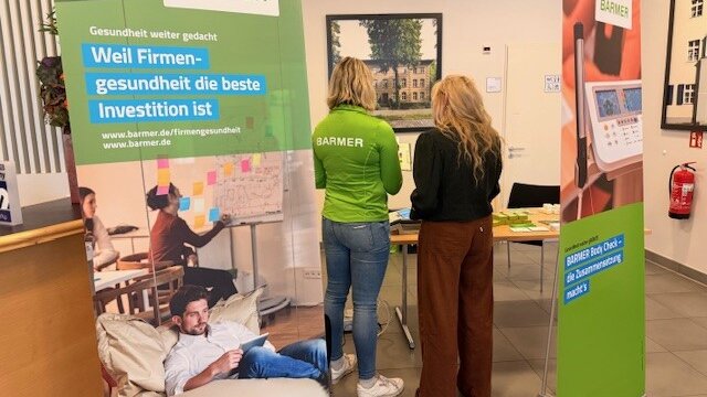 Eine Mitarbeiterin der Barmer und eine Mitarbeiterin von degewo stehen an einem Tisch und tauschen sich zu Gesundheitsangeboten aus.