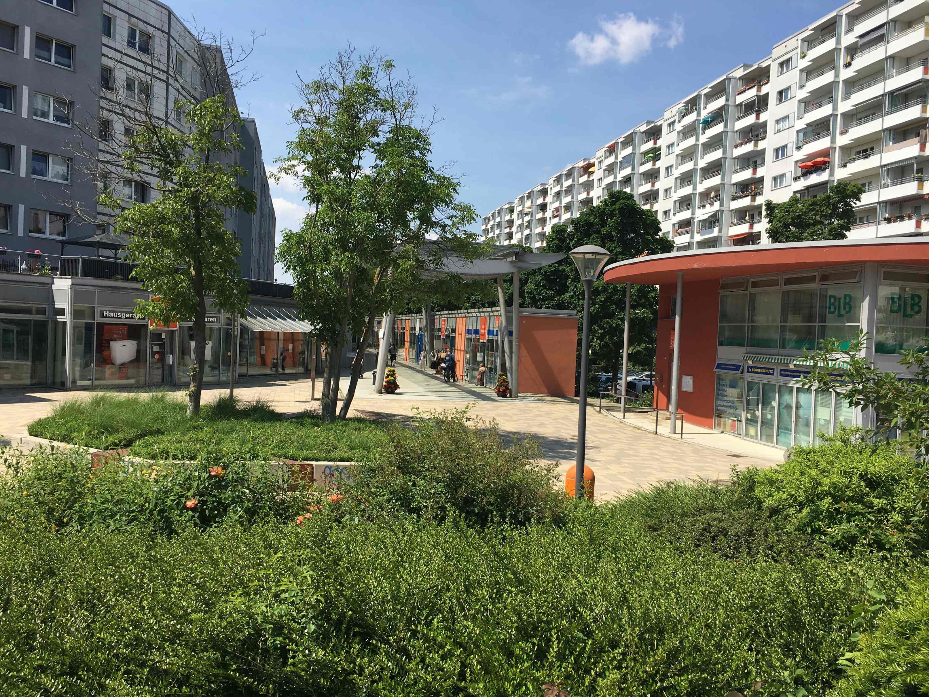 Die Promenade mit Bäumen, Büschen und Geschäften zwischen Hochhäusern