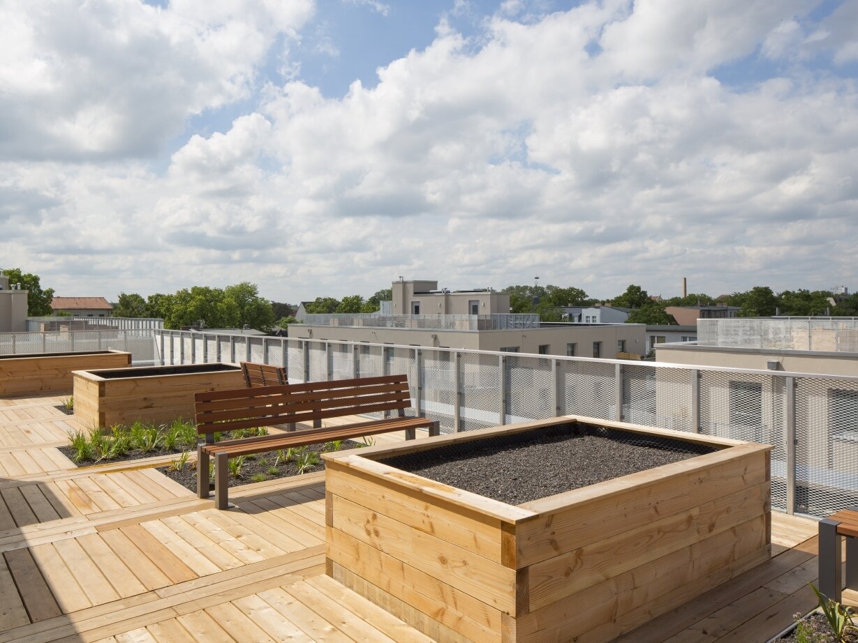 Außenansicht degewo-Neubau Karl-Pokern-Straße 30 bis 36: Terrassendach mit Hochbeeten und Sitzbänken.