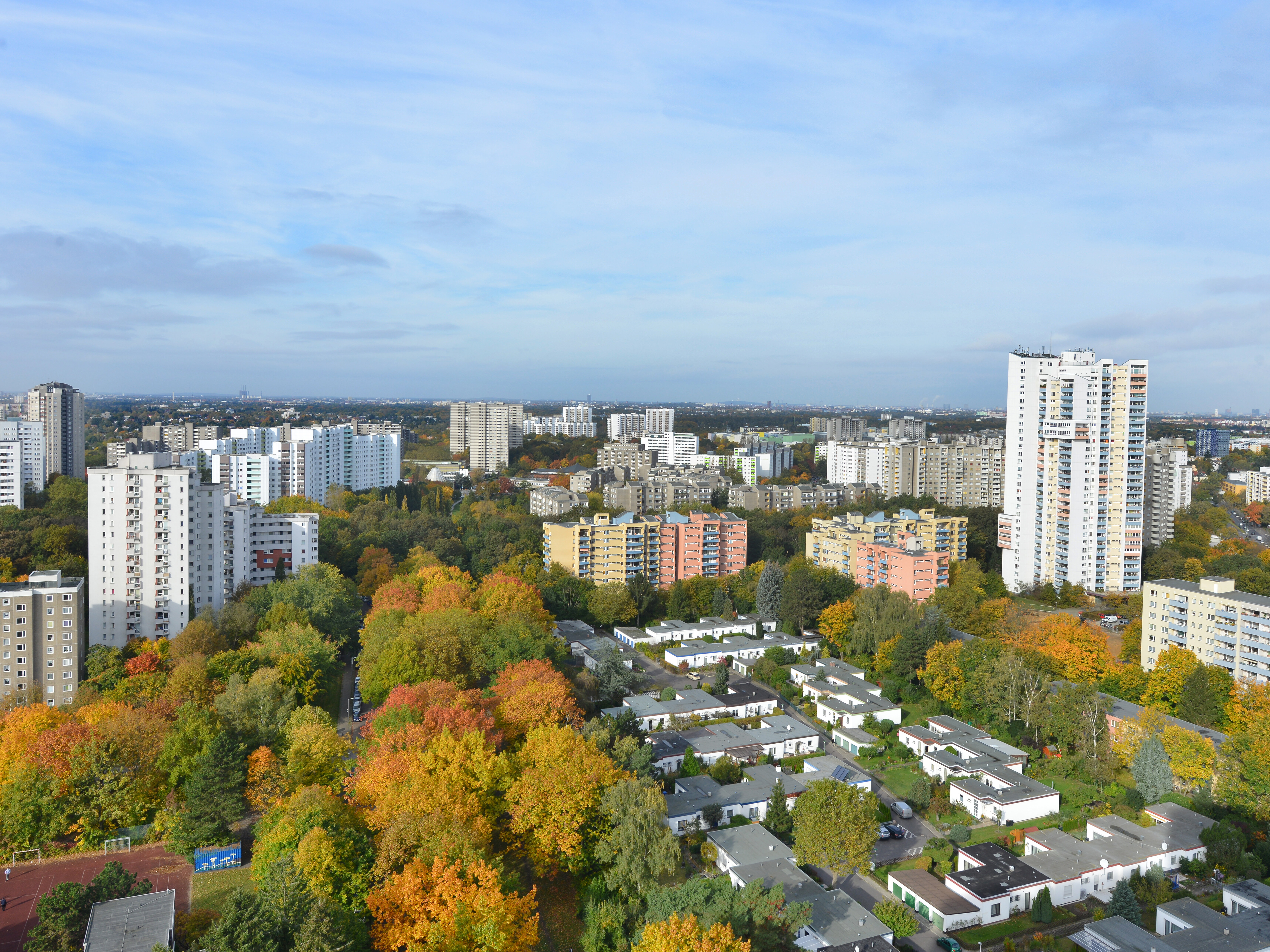 Panoramablick über die Gropiusstadt mit Hochhäusern, farbigen Wohnblöcken und herbstlichen Baumkronen.