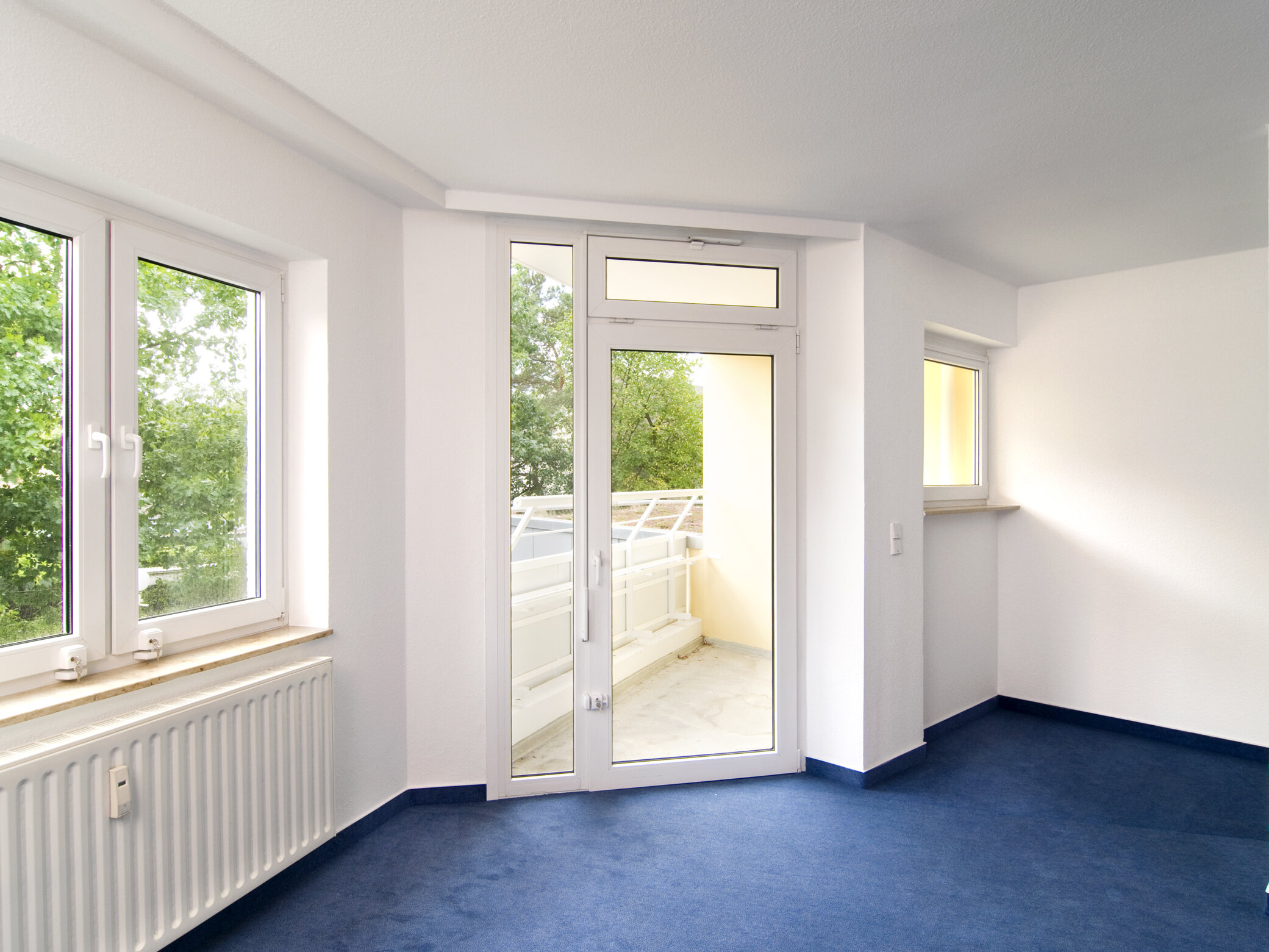 Leerer Wohnraum mit Blick auf Balkontür und Fenster