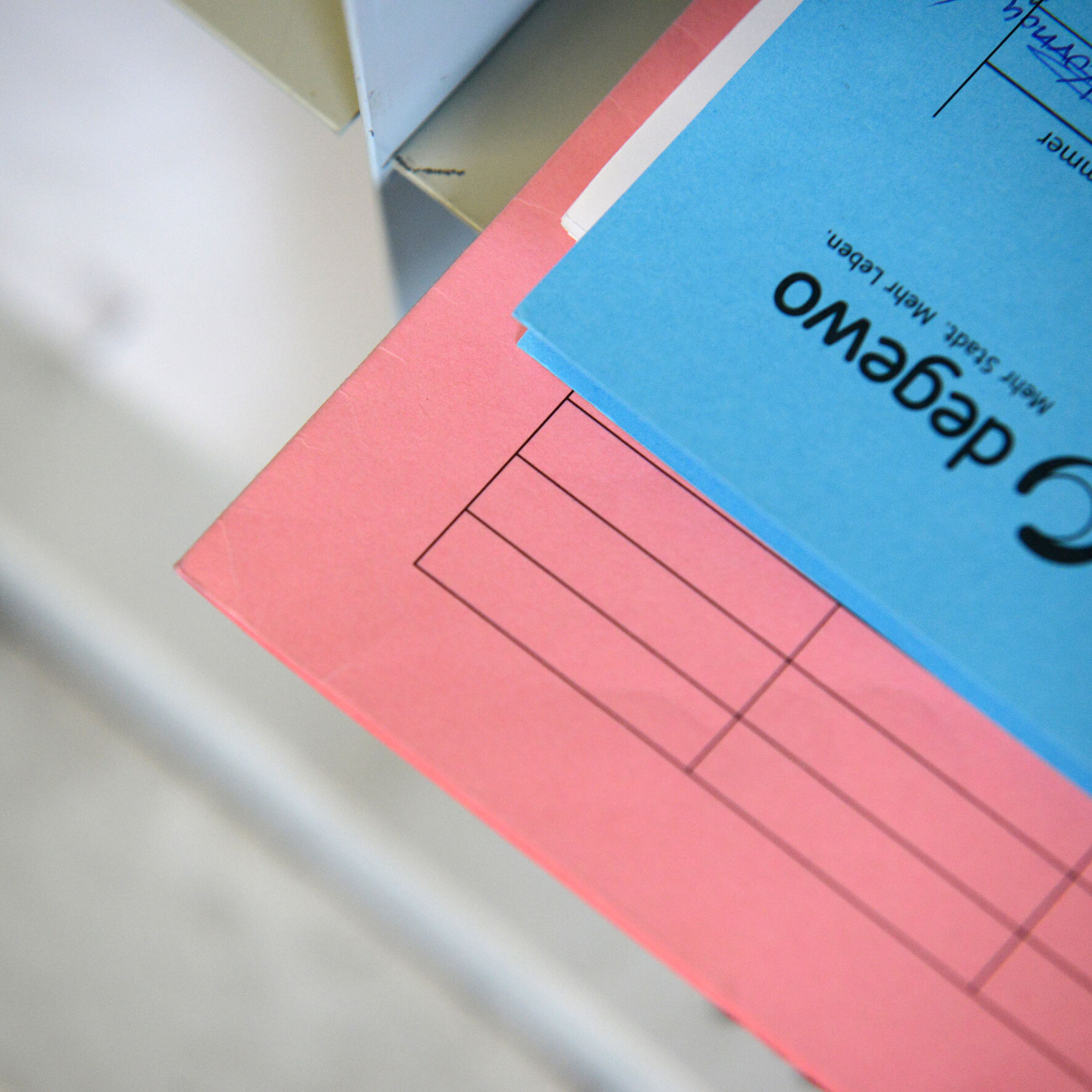 Nahaufnahme eines rosa und eines blauen Aktenordners mit degewo-Logo; der blaue Ordner liegt teilweise auf dem rosa Ordner, auf dem Deckblatt sind vorgedruckte Formularfelder und handschriftliche Einträge zu erkennen.
