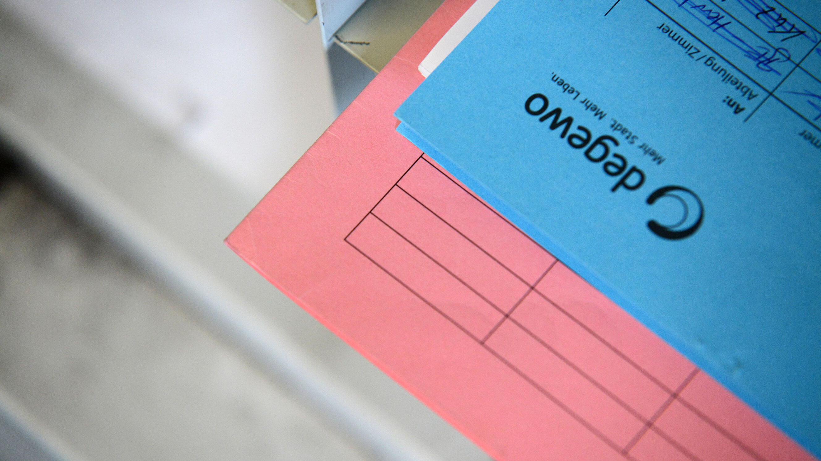 Nahaufnahme eines rosa und eines blauen Aktenordners mit degewo-Logo; der blaue Ordner liegt teilweise auf dem rosa Ordner, auf dem Deckblatt sind vorgedruckte Formularfelder und handschriftliche Einträge zu erkennen.