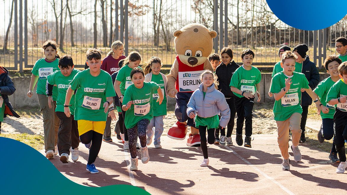Eine Gruppe Kinder rennt auf einem Sportplatz mit dem Maskottchen Berlino.