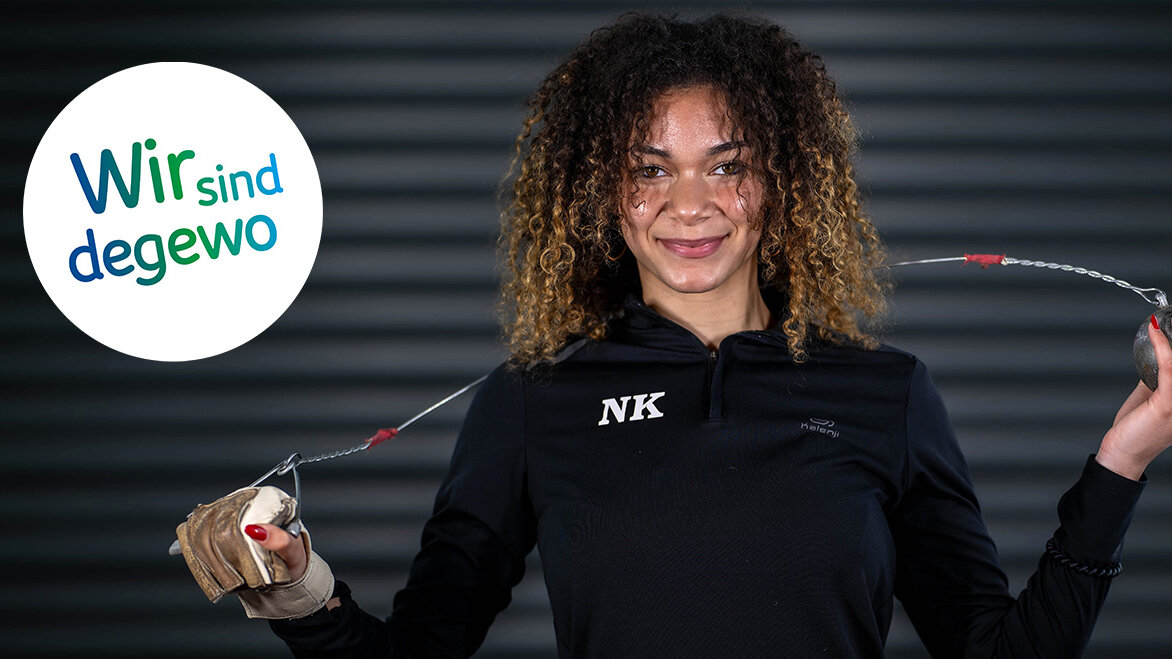 Eine junge Hammerwerferin hält einen Hammer in der Hand und lächelt in die Kamera.