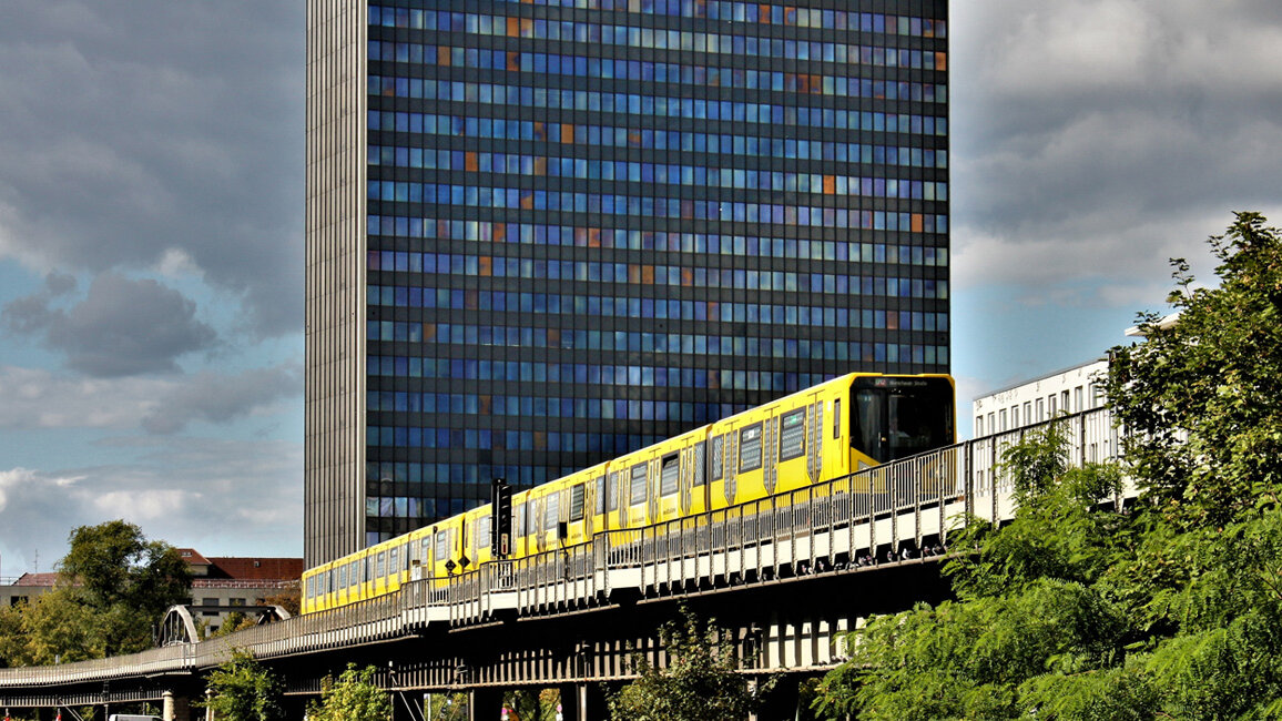 Eine gelbe U-Bahn fährt über eine Brücke. Im Hintergrund ein Hochhaus.