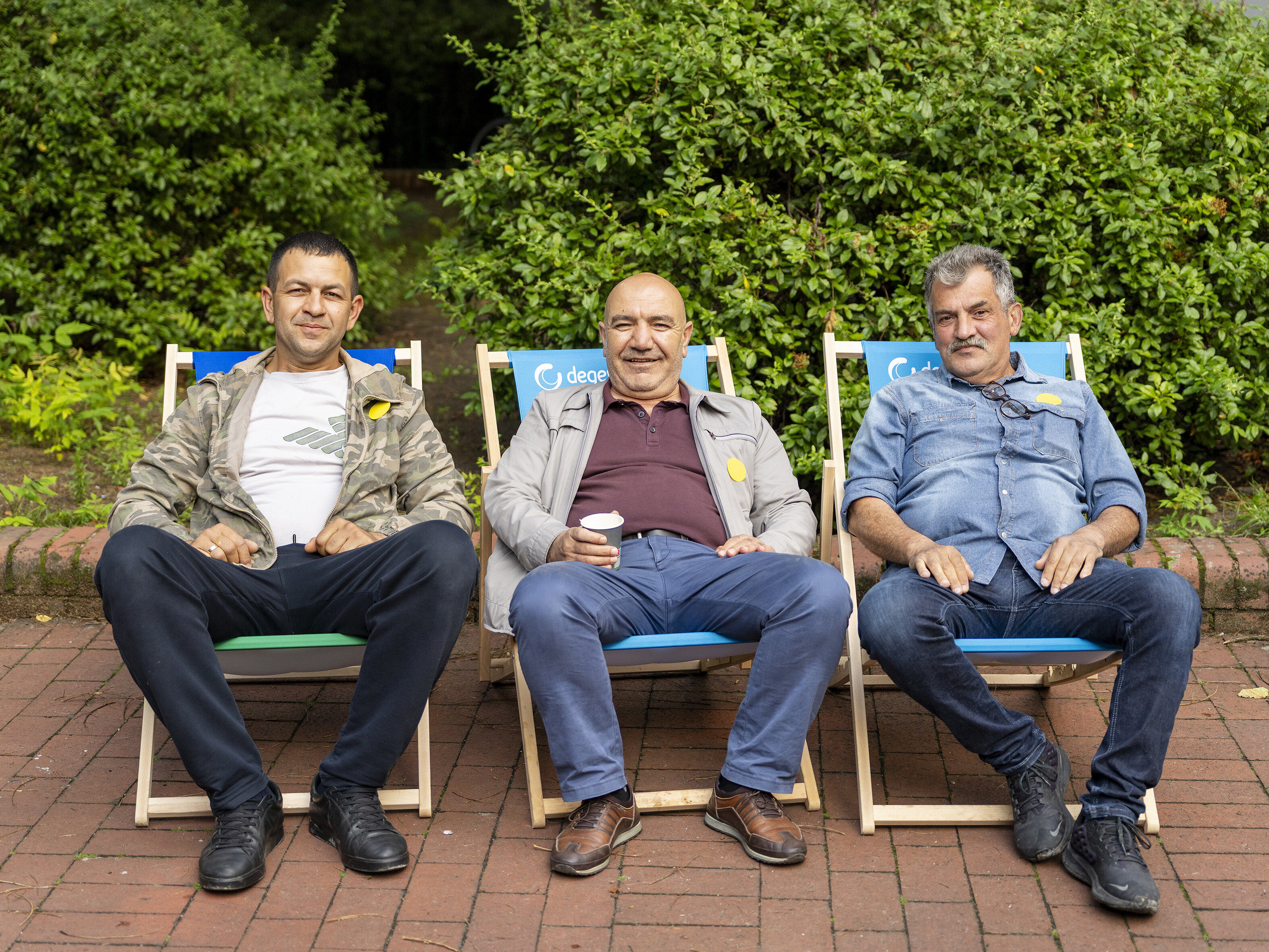 Drei Bewohner sitzen entspannt auf degewo-Liegestühlen im Innenhof und nehmen an der Beteiligungsveranstaltung teil.