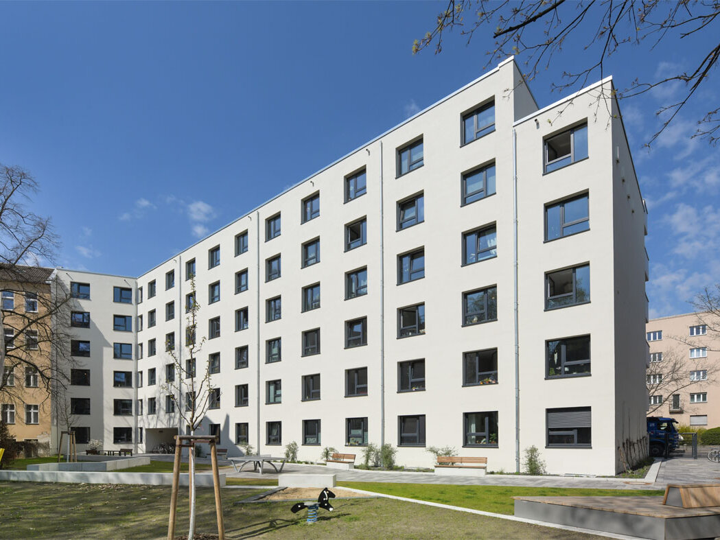 Außenansicht degewo-Neubau Steglitzer Damm 60: Hofseite mit Rasenspielplatz und neugepflanztem Baum im Vordergrund.