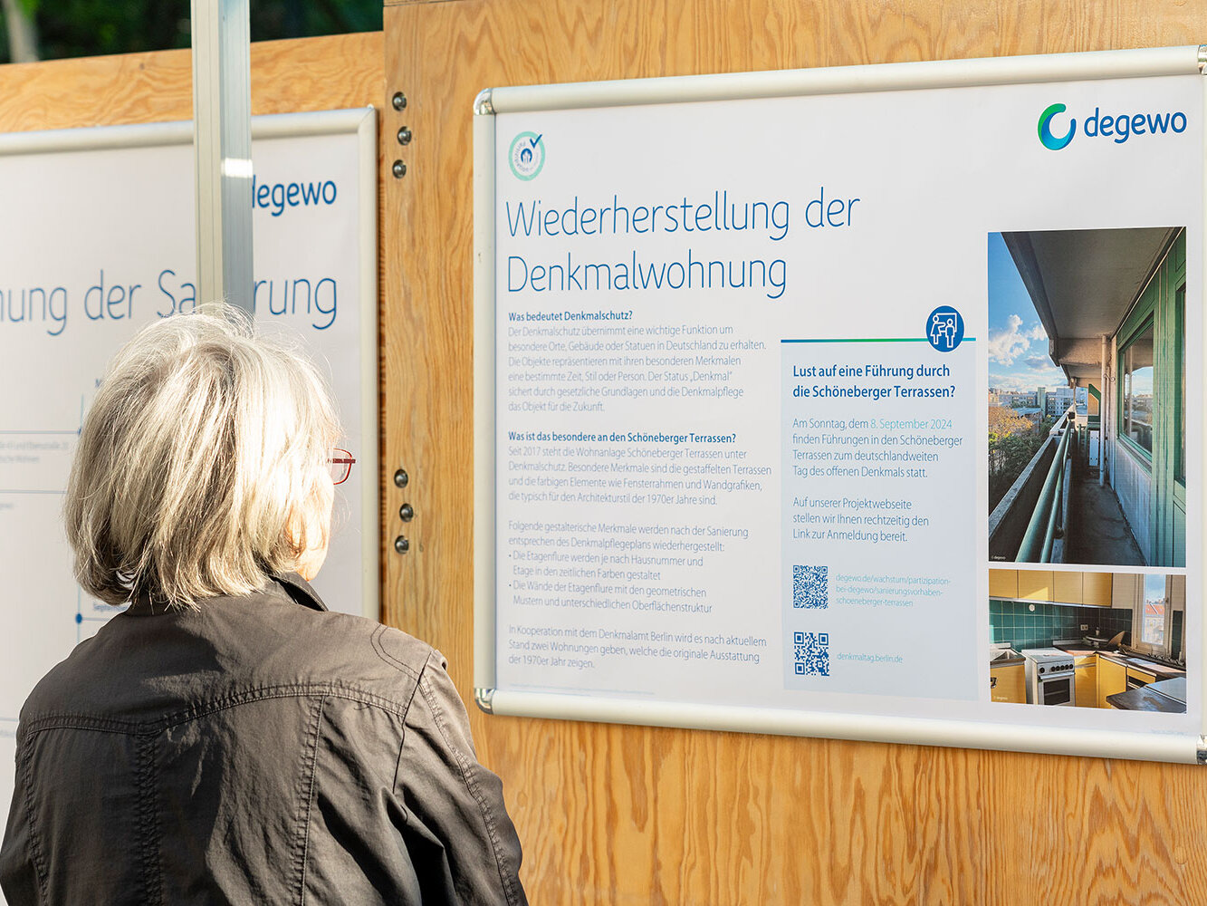 Besucherin betrachtet aufmerksam eine Infotafel mit dem Titel „Wiederherstellung der Denkmalwohnung“. Die Ausstellung informiert über Denkmalschutz, architektonische Besonderheiten der 1970er Jahre und geplante Führungen in den Schöneberger Terrassen.