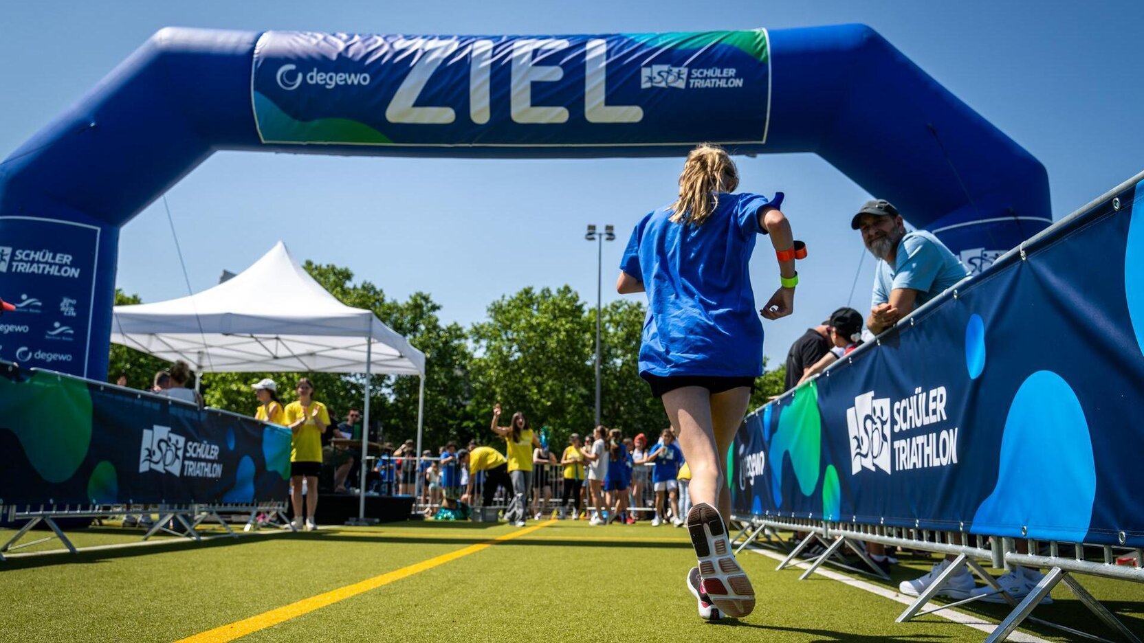 Ein Mädchen rennt über die Ziellinie bei einem Marathon. Dahinter steht Publikum und jubelt.