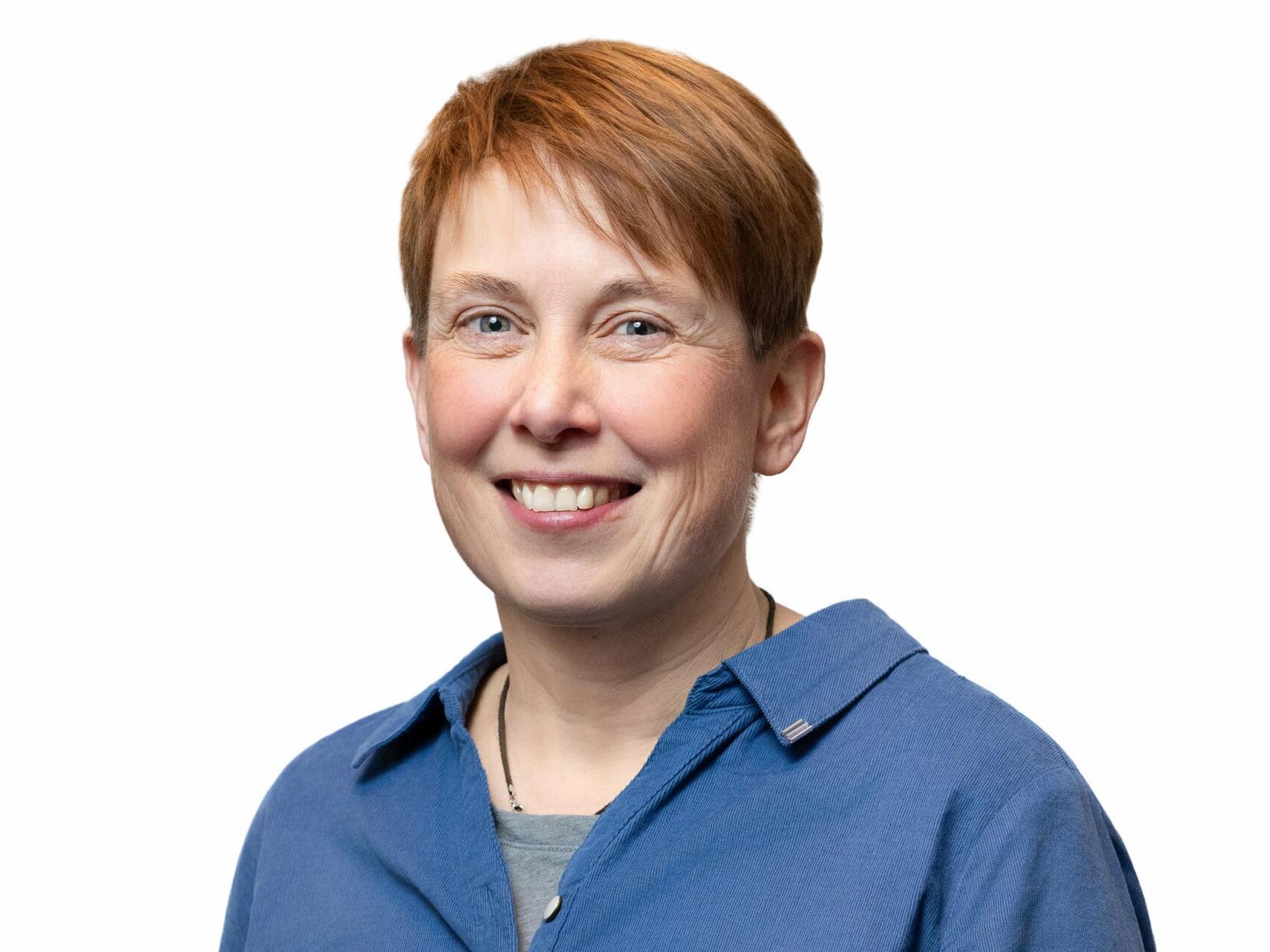 Eine mittelalte Frau lächelt freundlich in die Kamera. Sie hat kurze, rotblonde Haare und trägt ein blaues Hemd.