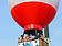 Mehrere Personen befinden sich in einem Heißluftballon. Dieser wird von einem Baukran in den Himmel hinauf gezogen. 