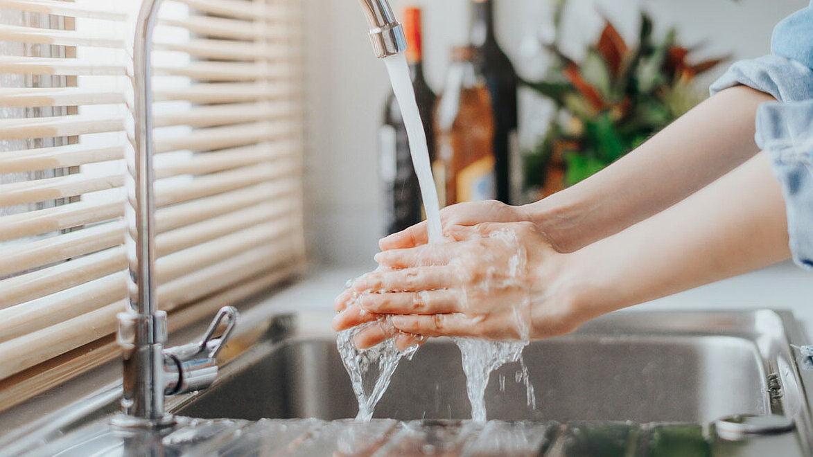 Person wäscht Hände unter laufendem Wasserhahn.