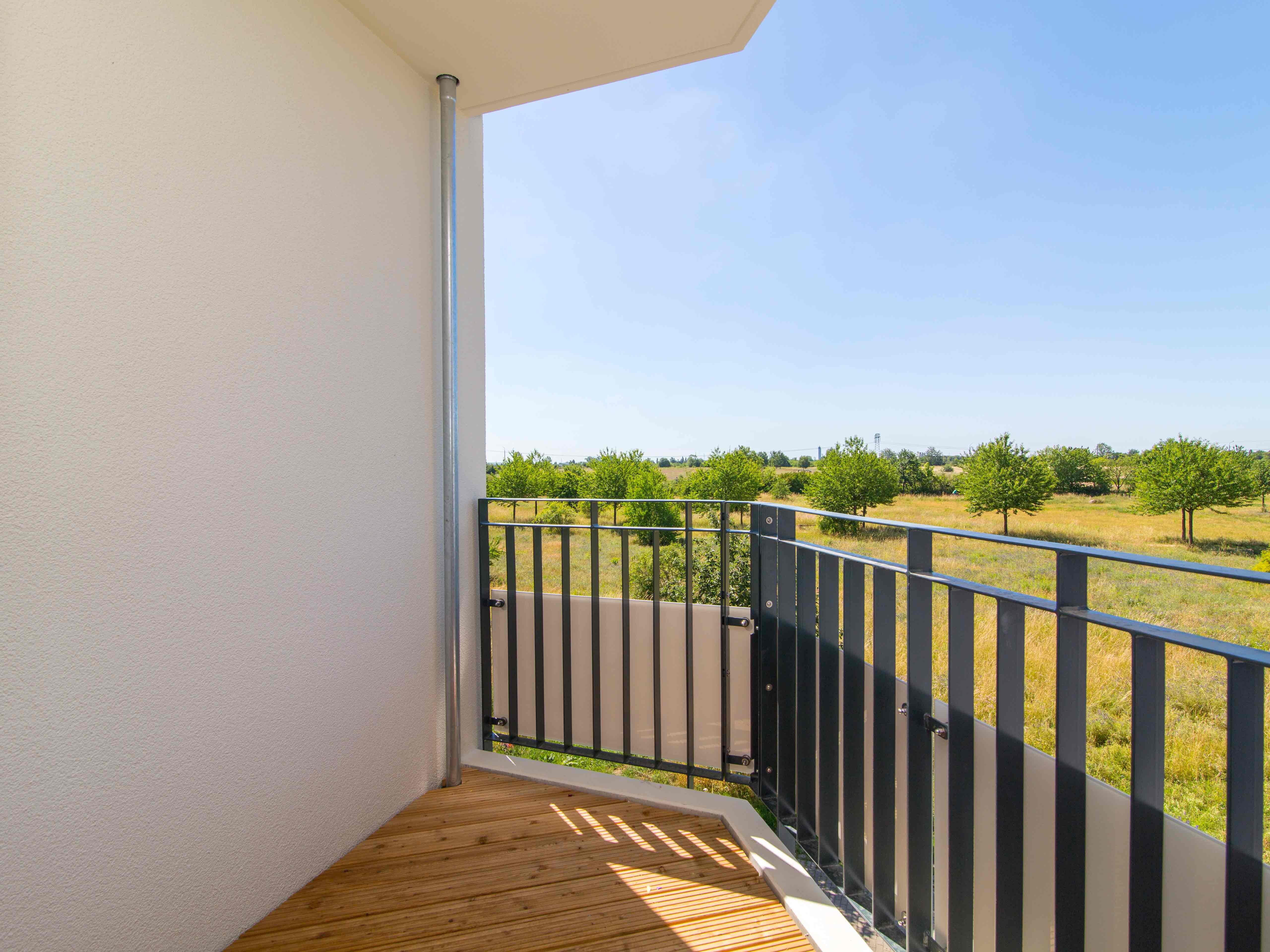 Außenansicht degewo-Neubau Elly-Heuss-Knapp-Straße 44: Blick von Balkon auf Grünfläche mit Bäumen.