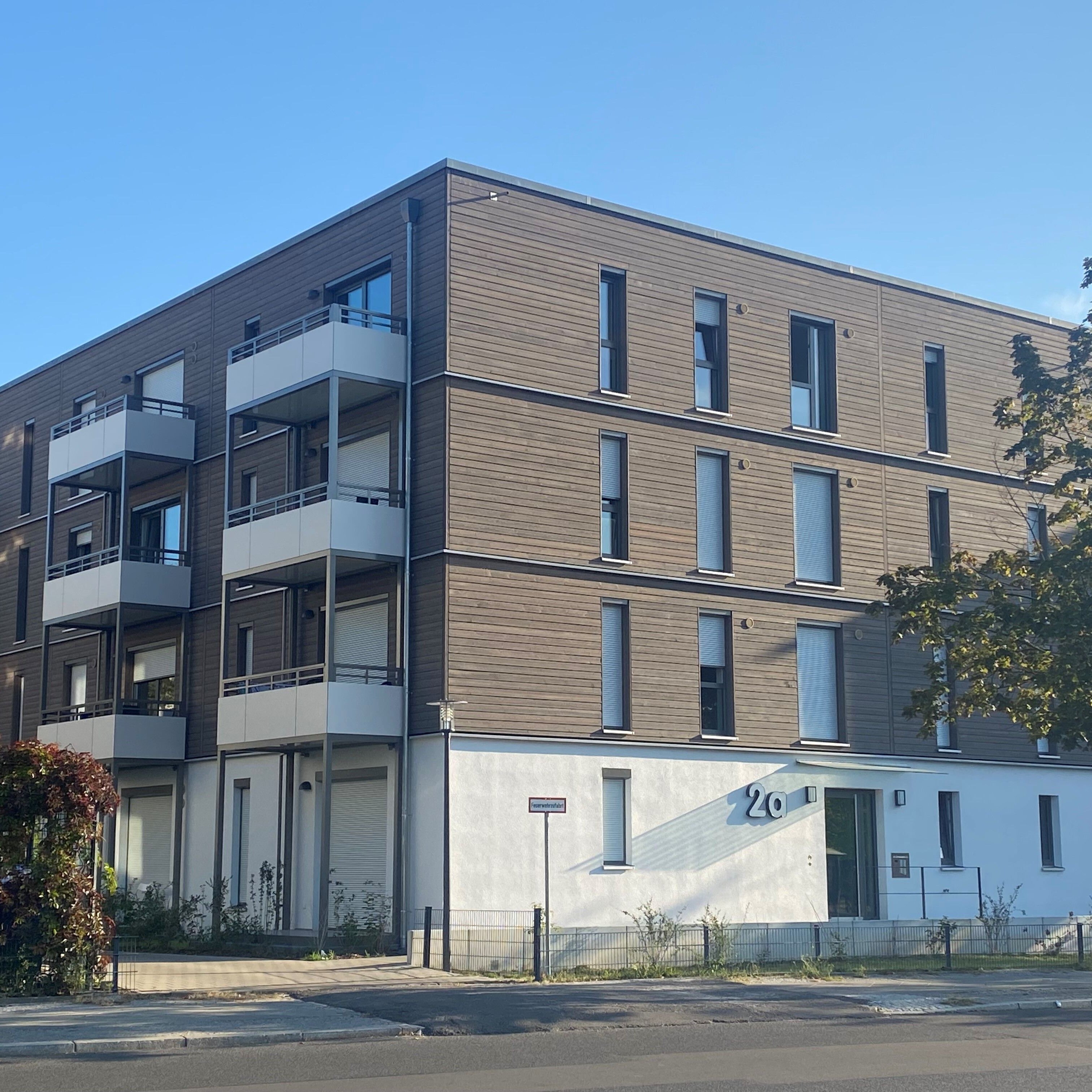 Mehrgeschossiges Wohnhaus mit moderner Holzfassade, weißen Balkonen und großen Fenstern in einem grünen Wohnquartier mit zeitgemäßer Architektur und nachhaltigem Anspruch.