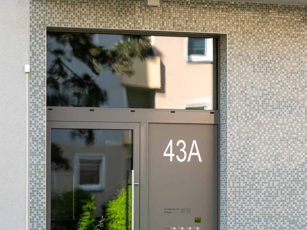 Außenansicht degewo-Neubau Borgenhagenweg 43A: Eingangsbereich mit Sträuchern und Fahrradständer im Vordergrund.