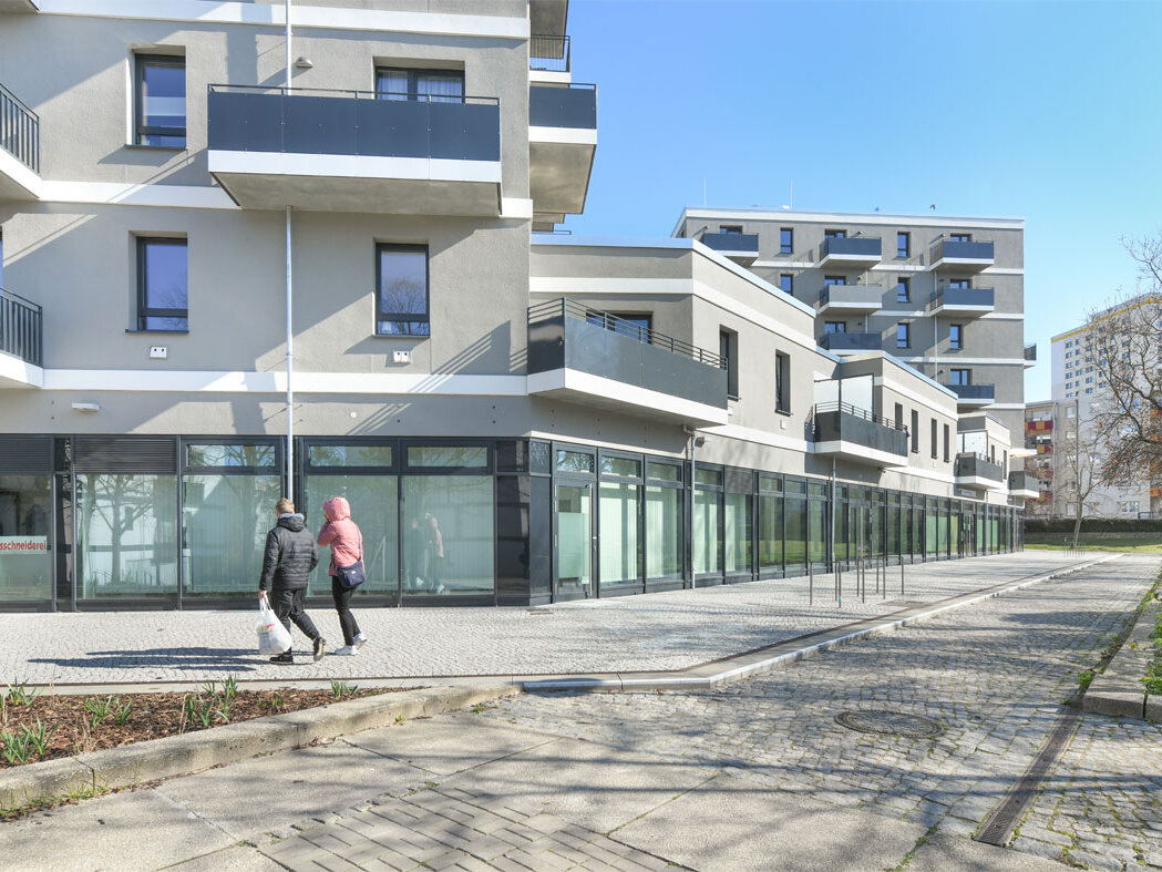 Außenansicht degewo-Neubau Mehrower Allee 28 und 30 mit Wegen und zwei Personen im Vordergrund.