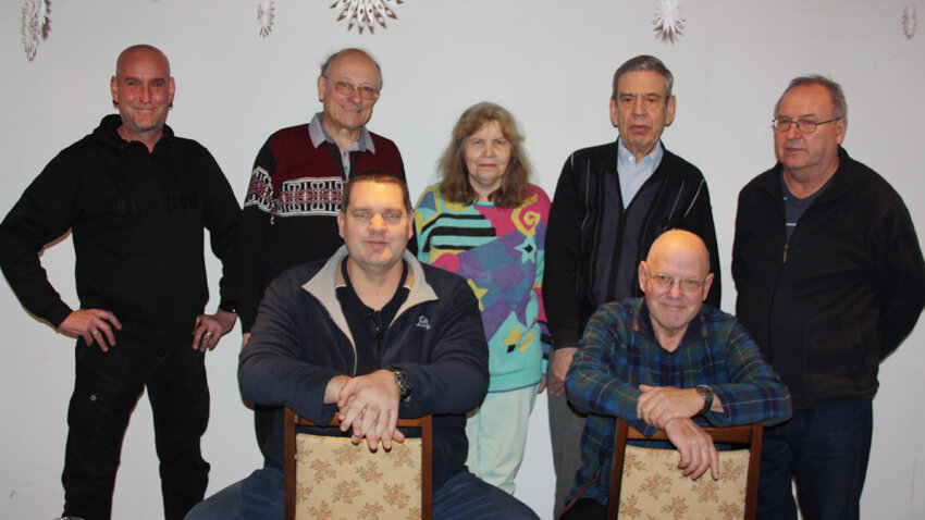 Gruppenaufnahme des Mieterbeirates Marzahner Promenade. Es sind 7 Mitglieder, die in zwei Reihen vor einer Wand stehen.