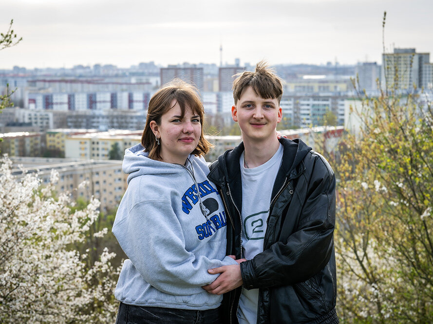 Ein junges Paar posiert auf einer Anhöhe. Im Hintergrund ist verschwommen das Berliner Stadtponarama zu erkennen.