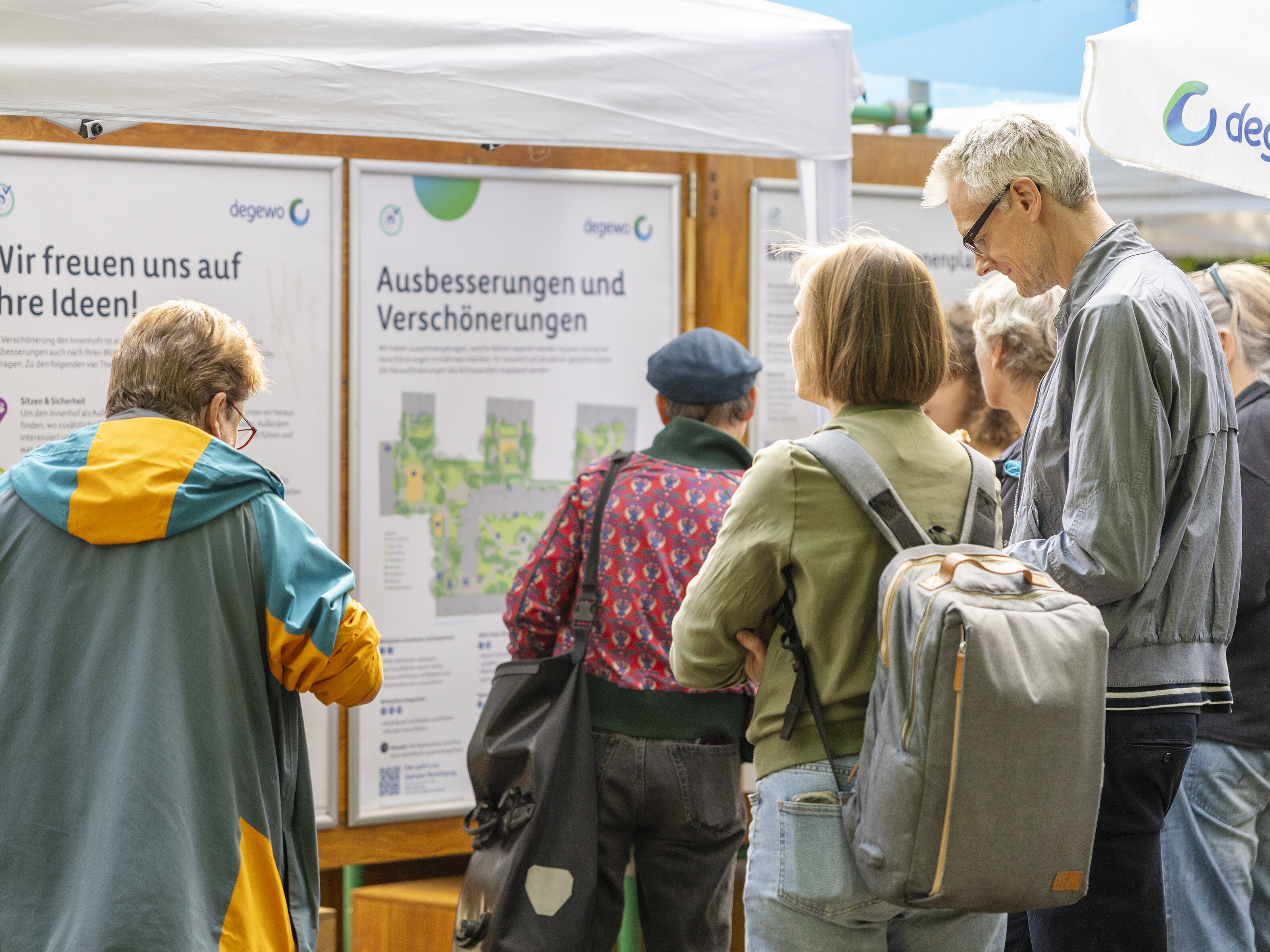Bewohnerinnen und Bewohner informieren sich an degewo-Stellwänden über geplante Ausbesserungen und Verschönerungen im Brunnenhof.