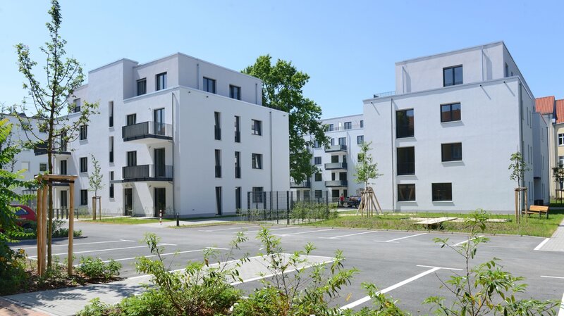 Hofansicht degewo-Neubau Klutstraße 22c mit neu gepflanztem Baum, Weg, Beeten und Parkplätzen im Vordergrund.