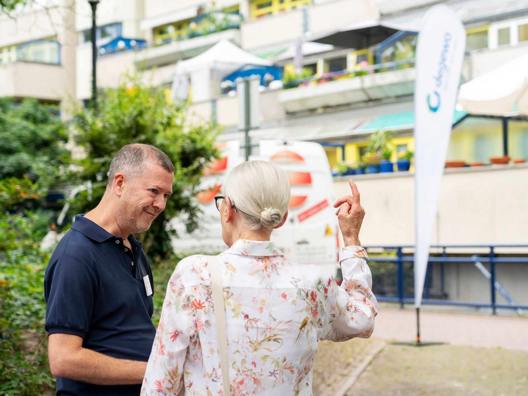 Eine Frau und eine Mann stehen vor einem Gebäude in der Schlangenbader Straße und unterhalten sich. 