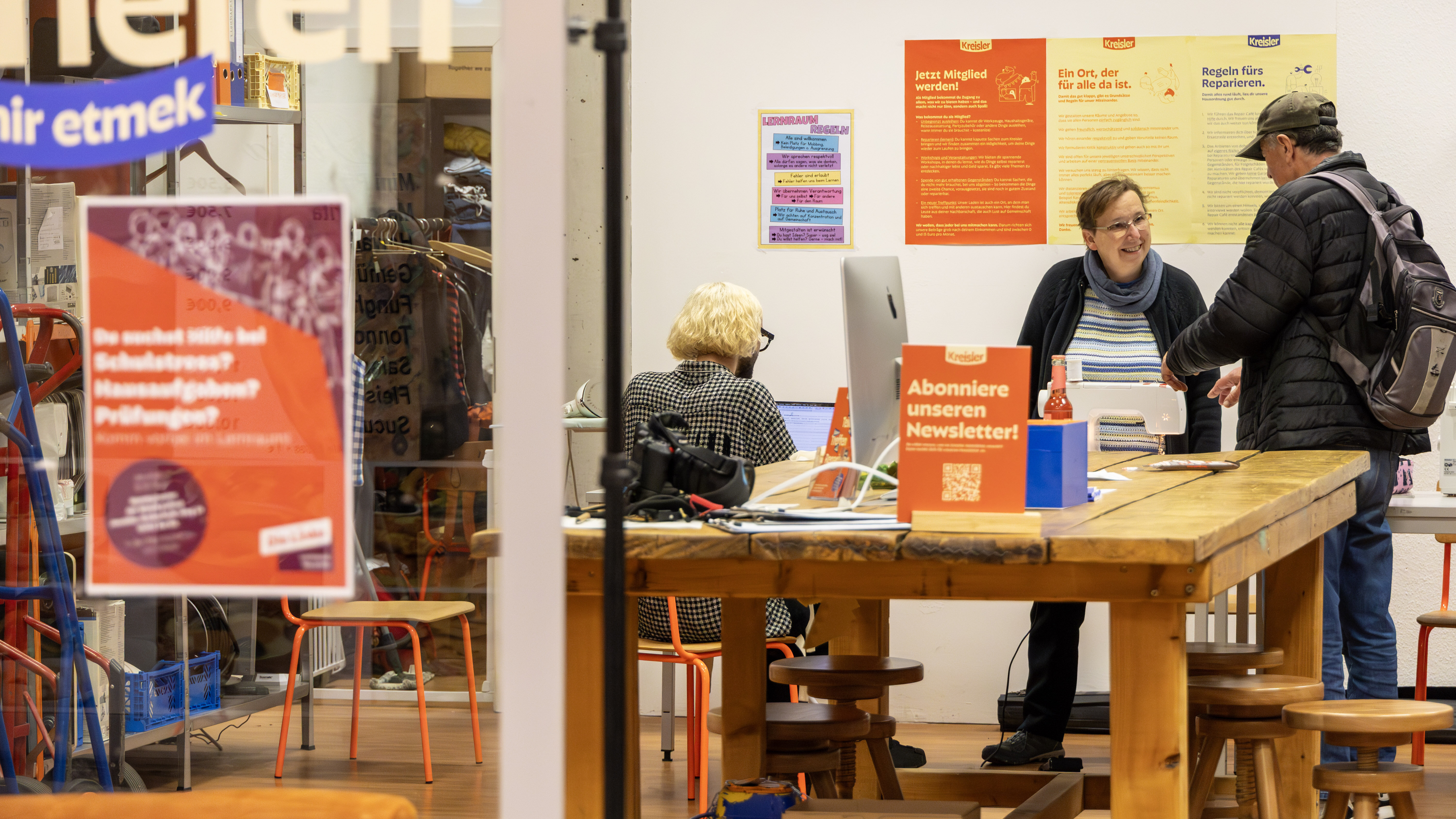 Frau berät Mann in einem offenen Werk- und Begegnungsraum mit Infoplakaten.