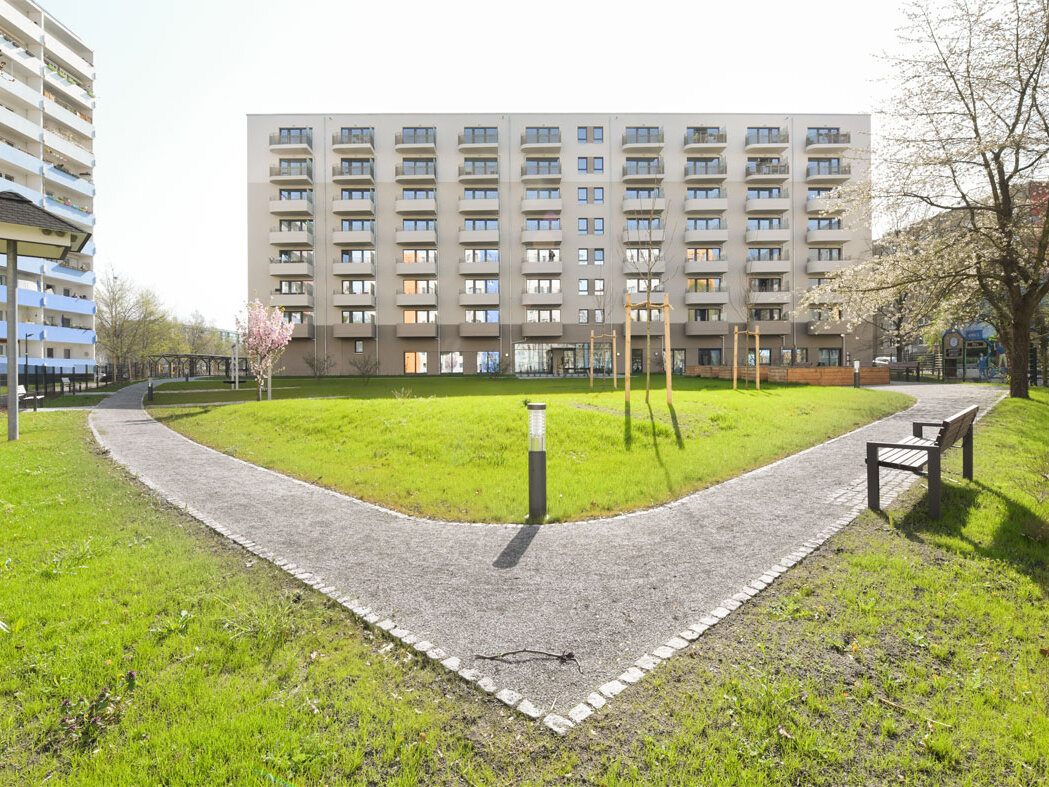 Außenansicht degewo-Neubau Venusstraße 28 mit Grünflächen, Weg, Weglaterne und Bank im Vordergrund.