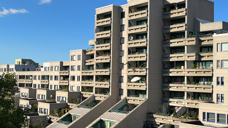 Außenansicht der Wohnanlage „Schöneberger Terrassen“ mit gestaffelten Gebäudeteilen, großzügigen Balkonen und bepflanzten Terrassen unter blauem Himmel.