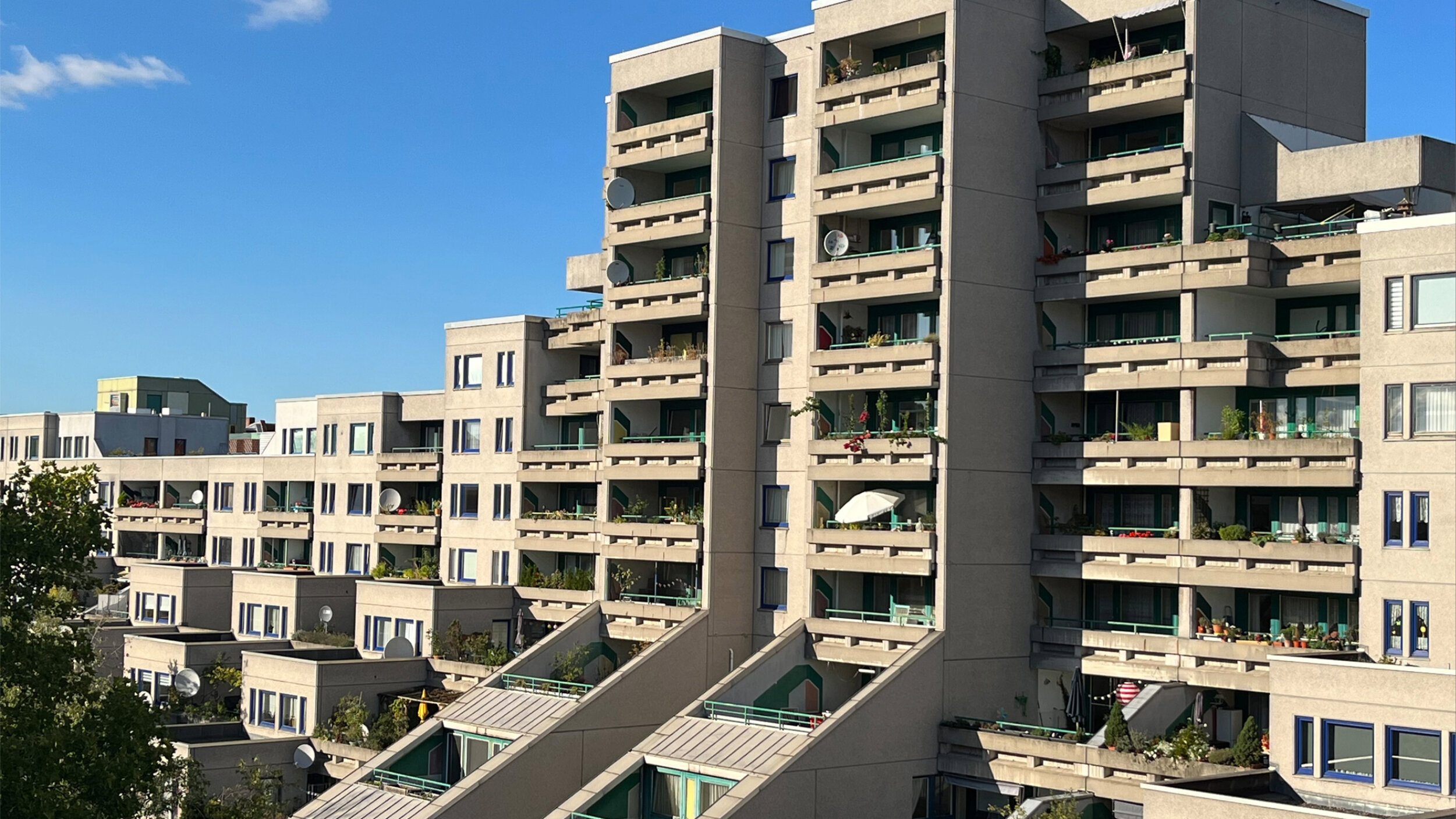 Außenansicht der Wohnanlage „Schöneberger Terrassen“ mit gestaffelten Gebäudeteilen, großzügigen Balkonen und bepflanzten Terrassen unter blauem Himmel.