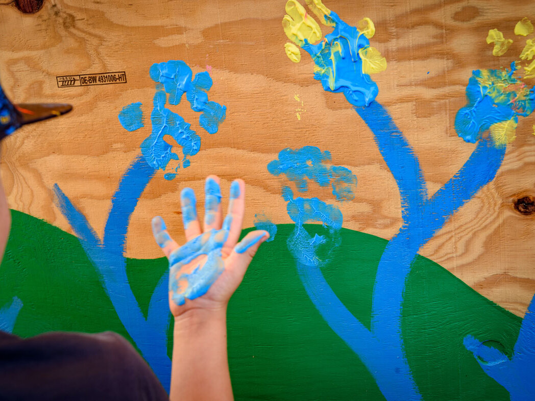 Detailaufnahme von bunten Handabdrücken mit blauer und gelber Farbe auf einer Holzfläche, entstanden bei einer kreativen Mitmachaktion für Kinder.