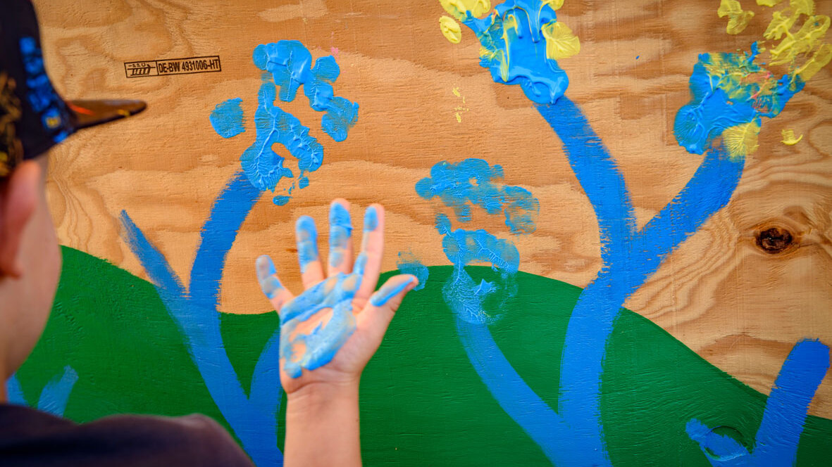 Detailaufnahme von bunten Handabdrücken mit blauer und gelber Farbe auf einer Holzfläche, entstanden bei einer kreativen Mitmachaktion für Kinder.