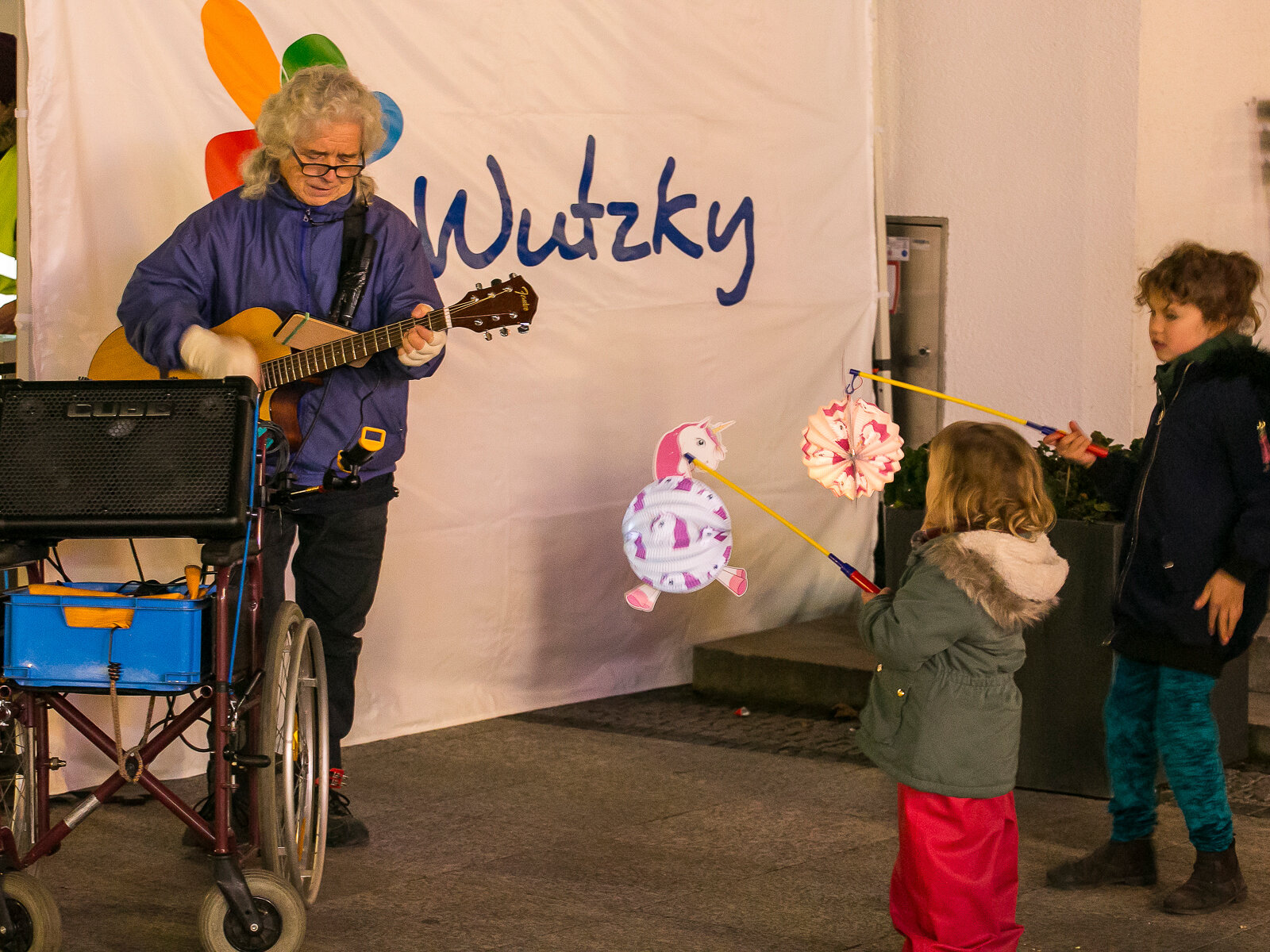 Jemand spielt Gitarre und Kinder mit Laternen schauen zu