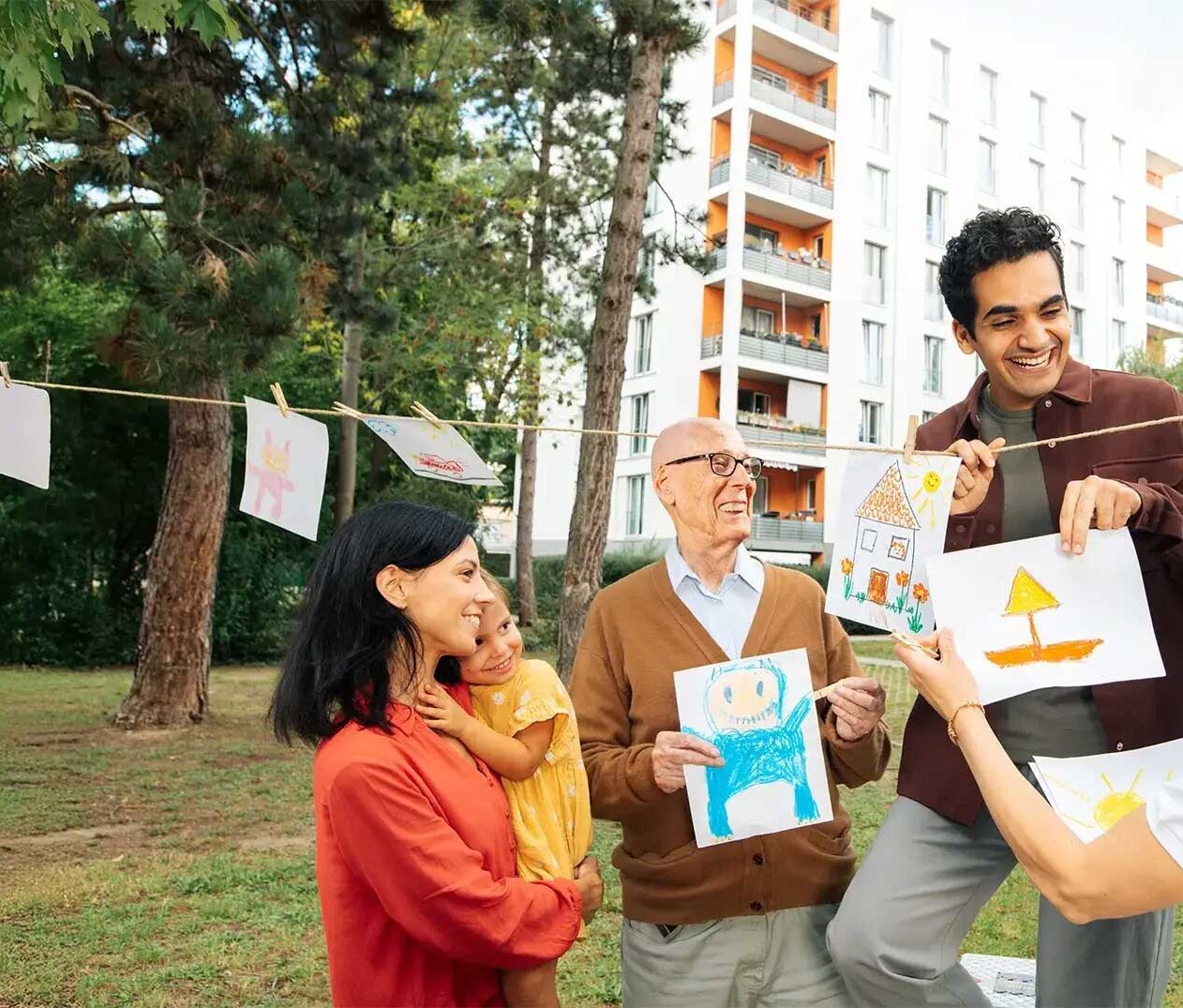 Eine Gruppe Mieterinnen und Mieter schaut sich gemalte Kinderbilder an. Sie sind im Hof und lachen. Im Hintergrund ist ein Mehrfamilienhaus zu sehen.