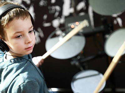 Ein Junge trägt Kopfhörer und spielt eine Trommel.