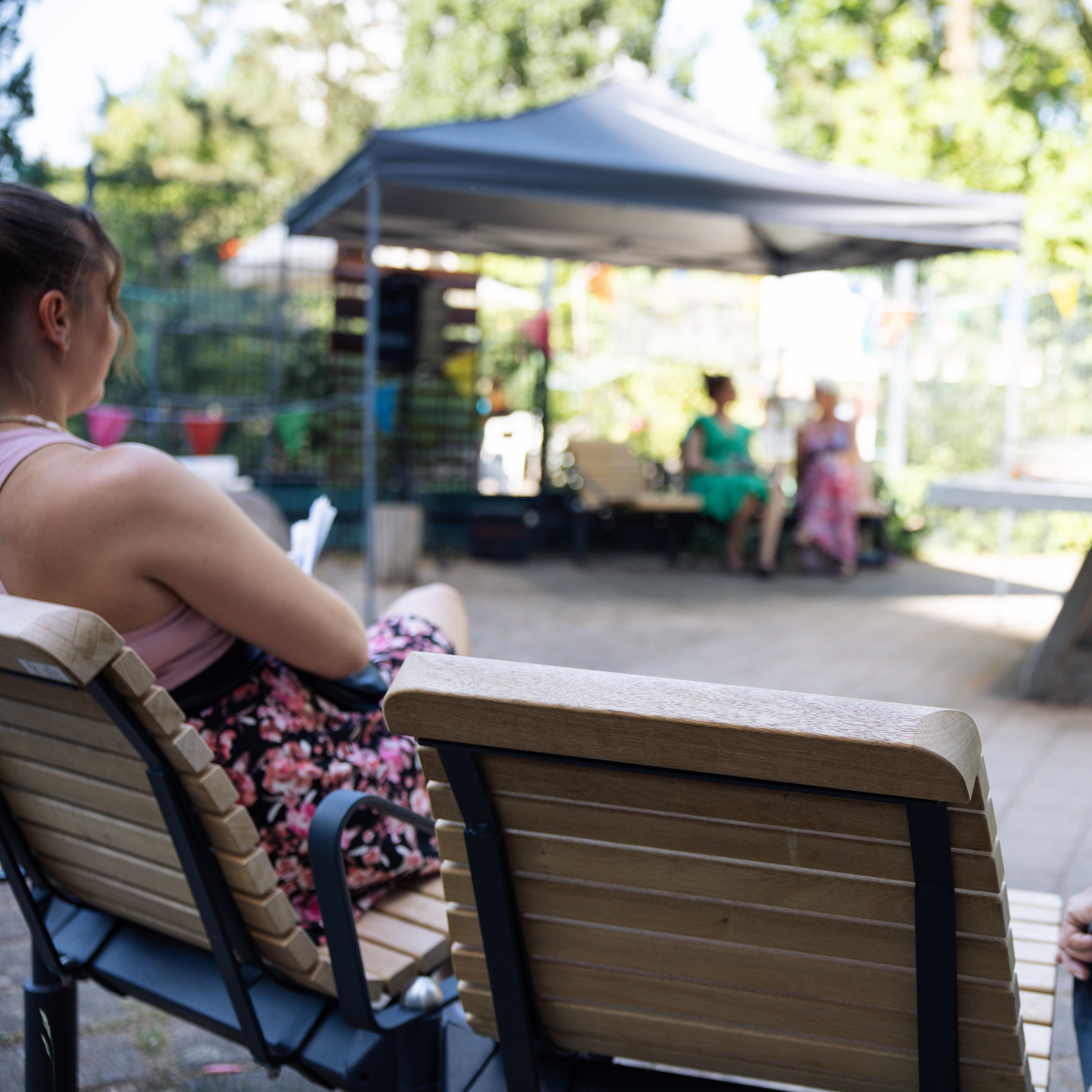 Blick von Hinten auf zwei Frauen, die auf einer Plauderbank sitzen. Im Hintergrund eine Tischtennisplatte und eine weitere Plauderbank.