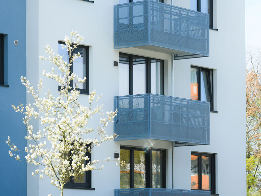 Außenansicht Fassade degewo-Neubau Pöhlbergstraße 9 Bärensteinstraße 5 mit Balkonen und blühenden Bäumen.