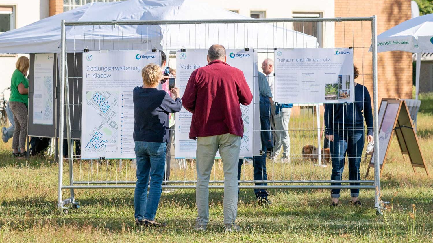 Mehrere Personen betrachten Informationsplakate zur degewo-Siedlungserweiterung in Berlin-Kladow auf einer Freifläche.