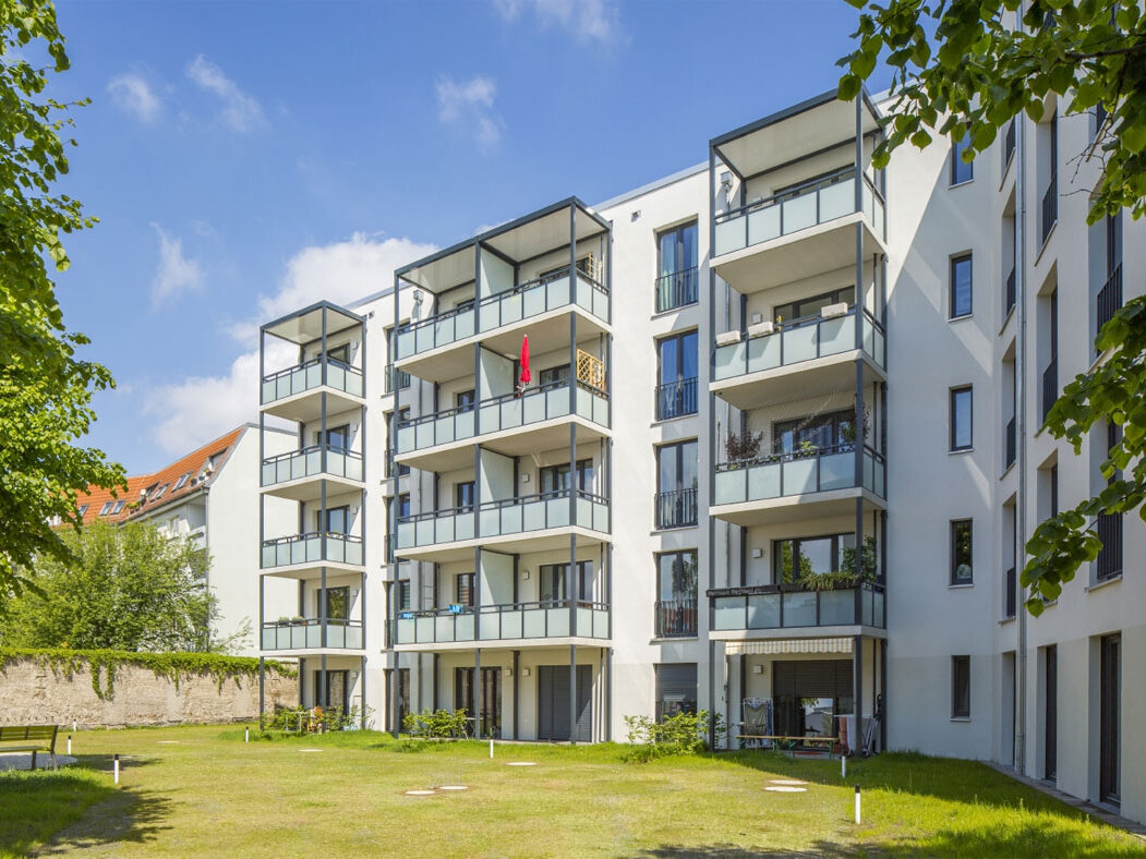 Außenansicht degewo-Neubau Luisenstraße 24 bis 24 A: Hofseite mit Grünfläche und beblätterten Zweigen links und rechts im Vordergrund.