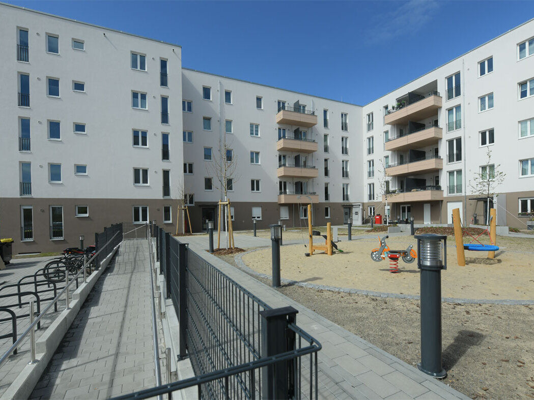 Straßenansicht degewo-Neubau Schwartzkopffstraße 20 bis 28: Hofseite mit Fahrradständern, Weg und umzäuntem Spielplatz.