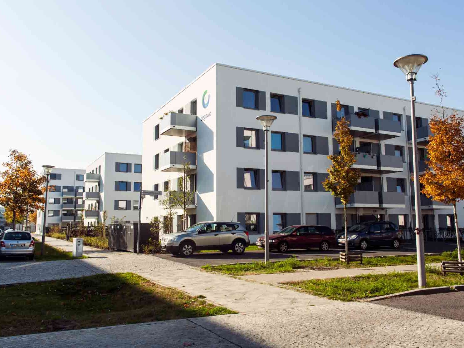 Straßenansicht degewo-Neubau Abram-Joffe-Straße mit Gehwegen, Straßenlaternen, Grünflächen und neu gepflanzten Bäumen im Vordergrund.